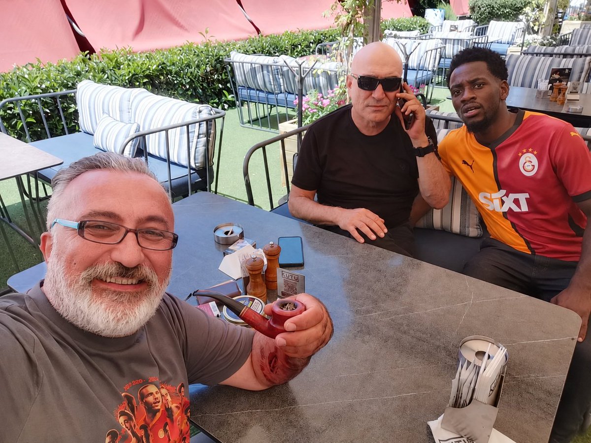 CagataySahin07's tweet photo. Bugün Kutu'da pipo keyfi yaparken içeri John Duran girdi.

Garsonlar kapıda görünce:

"Ooo Duran Emmi hoş geldin!"

diye karşıladı.

Geldi masaya oturdu. Bir yandan Galatasaraylı futbolcuların Instagram paylaşımlarını beğeniyor, bir yandan da bizim masadaki gözlüklü siyah tişörtlü abiye dil döküyor.

Dayanamadım sordum:

"Hayırdır John, mesele ne?"

Başını öne eğdi:

"Abi Allah aşkına, hiç mi faydam dokunmaz bu takıma?"

Dedim:

"Hangi takıma?"

İç çekti:

"Galatasaray'a..."

Sonra ekledi:

"Logosunda maydanoz olan takımda oynayarak bir cahillik yaptım. Rabbim affetsin."

Bu sırada gözlüklü abinin kolunu tuttu:

"Abi ne olur bir konuşun, bir referans olun, valizim hazır. Torreira'yı beğendim, Sara'yı beğendim, Yunus'u beğendim... Daha ne yapayım?"

Garson uzaktan seslendi:

"Duran Emmi, sen kafayı çoktan Galatasaray'la bozmuşsun!"

John sadece gülümsedi... 😄

Sizce John Duran gerçekten Galatasaray forması giyerse ligde kaç gol atar? 👇🟡🔴