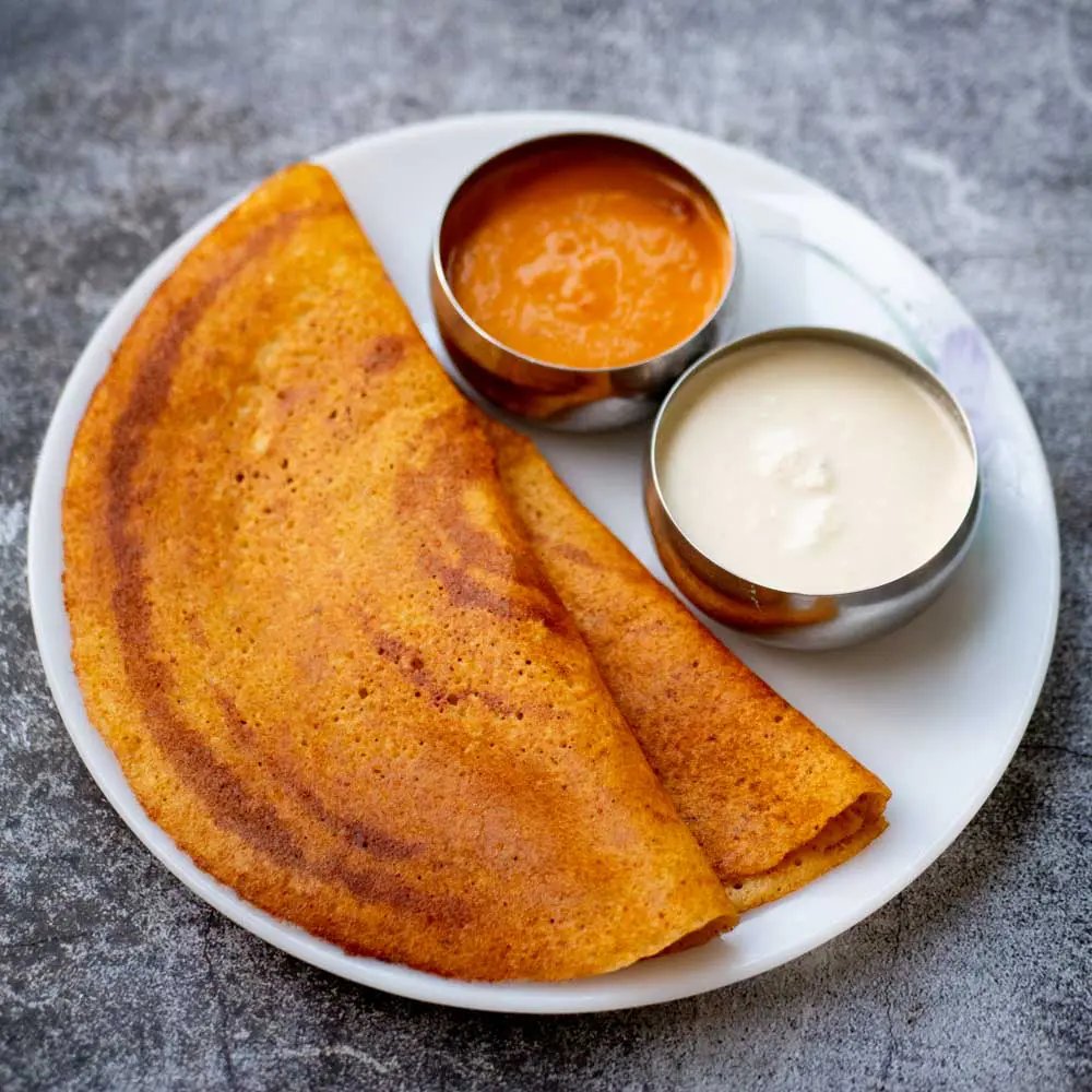 Fintech03's tweet photo. With Indian IT being the topic of the week, I thought it was only fair to trace the origins of the food that has probably powered more code, daily standups & production fixes than anything else: the dosa. 

The history of the Dosa is a fascinating journey through time. What we eat today as a golden, paper-thin crepe was originally an ancient, rugged, protein-heavy pancake that relied completely on the structural biochemistry of an "aristocratic bean." The historical timeline highlights how the different regional iterations: Dosai, Thosai, Adai & Dosaka evolved over 2 millennia across South India.

The earliest references to Dosai (often spelled thosai/tocai) emerge from ancient Tamil Sangam literature. In this era, it was far from a delicate breakfast item. There were no flat iron tawas. Ancient Tamils cooked the batter on heavy, porous earthen clay platters/flat stones over open wood fires. Because clay plates retain uneven heat, spreading a batter thin was physically impossible.

Interestingly, the official status of the dosai was a non-fermented/minimally fermented pan-bread. It relied completely on the stickiness of the beans to bind the coarse grain together. It was dense, thick & highly filling, designed to sustain farmers & soldiers.

Running parallel to the early dosai was the Adai. Mentioned in the classic Sangam poem Madurai Kaanji, street vendors in the ancient city of Madurai sold these thick, griddled cakes to evening crowds. Unlike the dosai, which eventually streamlined into a rice & urad dal pair, the Adai retained its primitive, hyper-nutritious form. It used a combination of whatever lentils were on hand, pounded coarsely with red chilies & curry leaves & skipped fermentation entirely to provide immediate, heavy-duty protein release.

When the dish migrated into the royal Sanskrit texts of the Deccan region, it underwent a luxury upgrade. King Someshvara III compiled the Manasollasa, where he officially recorded the recipe for Dosaka:

Finely split, dehusked black gram (Masha) stone-ground into a velvety paste + Seasoned with asafoetida (hing), cumin, salt, and ginger juice + Cooked on a hot iron pan, then drenched in whole milk, ghee, & saffron.

The Dosaka was essentially a pure black gram cake. The royal chefs realized that if you whip urad dal paste vigorously, its proteins trap air bubbles naturally, giving you a soft, plush, cloud-like texture w/o needing an overnight rise.

If the ancient dosai & dosaka were thick, soft & spongy, how did we get the paper-crisp restaurant dosa? That change is a masterclass in food chemistry, pioneered by the cooks of Udupi, Karnataka, in the late 19th & early 20th centuries.

To achieve maximum crispiness, Udupi cooks radically flipped the grain math. They slashed the % of urad dal & spiked the batter with polished white rice & a handful of poha (flattened rice)/methi (fenugreek) seeds. When this rice-heavy, long-fermented batter hits a blazing hot, oiled iron tawa, the water vaporizes instantly. The starches in the rice undergo gelatinization & subsequent dehydration, locking into a rigid, brittle, wafer-thin matrix.

To summarize, the word dosa is not a modern invention, it describes a 2000 yr old evolutionary branch of South Indian culinary science. It started as a thick, sustaining bean-bread cooked on clay pots, transformed into a decadent, milk-infused delicacy for Chalukyan kings & was eventually re-engineered with high-starch physics by Udupi chefs to become the thin, golden, globally recognized icon it is today.