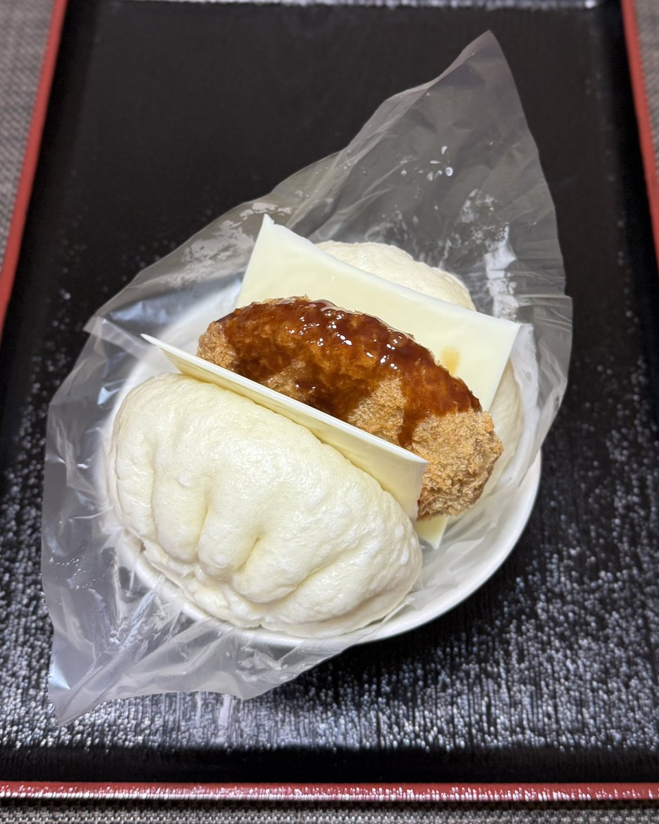 ITABASHI2929's tweet photo. 昼ごはん。「コロッケサンド！」セブンイレブンの大入り豚まんにレジ横の揚げ惣菜 ほくじゃが 牛肉コロッケ（塩胡椒）を挟むだけ。チーズ入れて合計1,000kcalオーバー！おにぎりぽっけに包むとこぼさず食べやすい。誕生日だからカロリーなんて気にしない。いただきます。 https://t.co/j1WOzkieZ0