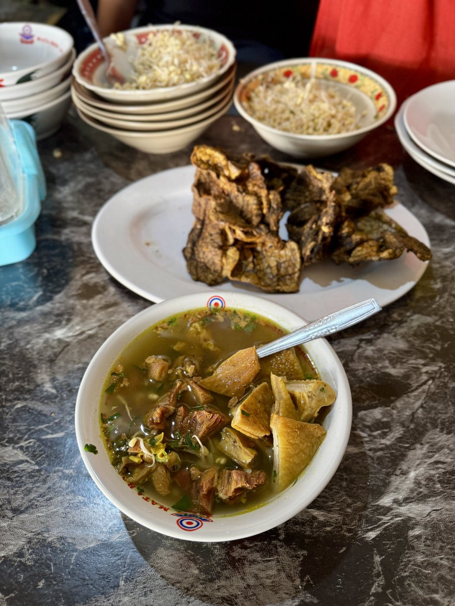 masakpartikelir's tweet photo. Soto Daging Sapi Pak Syamsul “LEJAR”, Pasar Colombo

Salah satu soto “unik” yang mewarnai persotoan duniawi di Jogja. Kuahnya tidak bening, mirip gagrak Lamongan tapi tanpa koya. Kaldunya dibuat dari bagian sandung lamur dan sengkel sapi. Kejutannya ada pada taburan bawang putih goreng. 

Isiannya sederhana saja. ￼ Nasi, tauge, daun seledri, dan daging. Standar. Yang tidak standar ada di lauk tambahannya.

Ada otak sapi goreng yang dibalur telur. Babat iso. Perkedel. Tempe garit kriuk. Semuanya lezat dan kenyal. Kondimen ada sambal yg agak encer, kicap manis, irisan jeruk nipis, dan lada.

Tempatnya cukup nyempil di sisi luar Pasar Colombo. Di antara toko buah dan toko makanan ringan. ￼ Tidak ada papan nama besar, tidak ada dekorasi. Kalau tidak tahu persis lokasinya, mudah kelewatan. Suasananya pasar betul, pembeli lalu-lalang, samar-samar terdengar suara tawar-menawar. ￼ Makan di sini terasa seperti ketidaksengajaan yang menyenangkan.

Arti kata LEJAR menurut abang yg jual adalah berkeringat kenikmatan saat menyanyap hidangan. 

Harganya liat sendiri ya, mau rate MBG atau mewah, monggo.

Sudah nyoto belum?