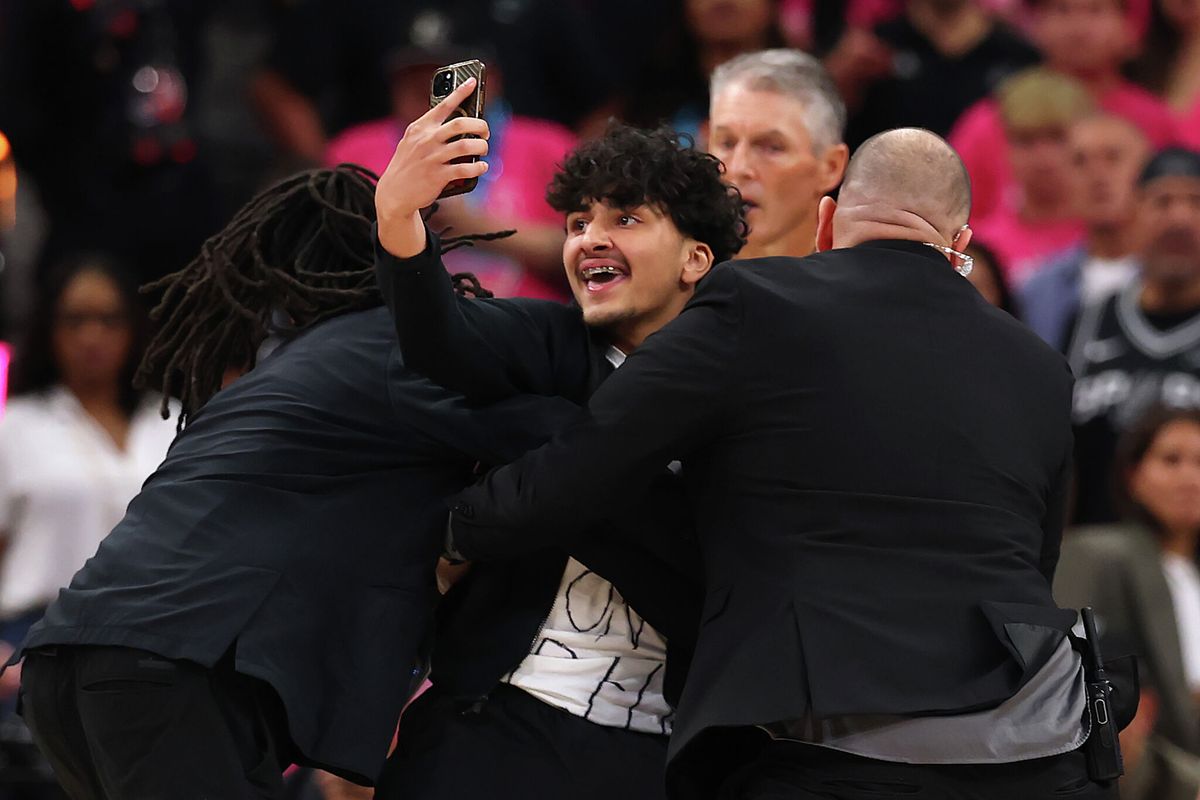 mySA's tweet photo. A fan rushed onto the court during the Spurs Finals game Wednesday night and filmed himself taking a selfie with Wemby. 🤭 That's got to be a lifetime ban, right? 🔗 https://t.co/NMAhVmtrS4 https://t.co/dvfTVvZ49t