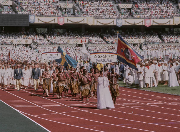 Darkmatterh6nd's tweet photo. Long jumper Sizwe Sydney Mdluli leads the team from the Kingdom of Swaziland bearing the national flag during the Olympic Parade Of Nations at the opening ceremony for the XXIV Olympic Summer Games on 17th September 1988 at the Seoul Olympic Stadium in Seoul, South Korea. https://t.co/j32WnqCtkK