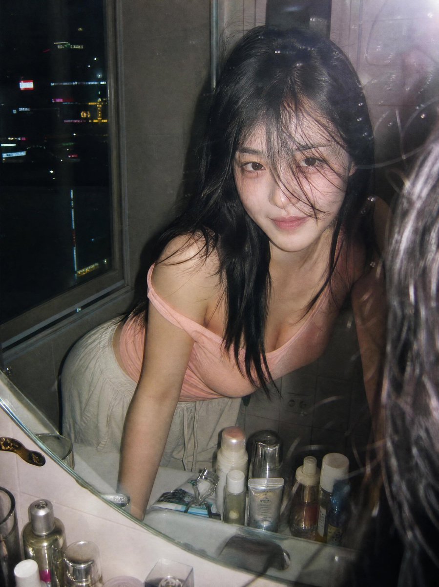 jzaib4269's tweet photo. Created with GPT Image 2.0 on Yapper 

Prompt: Ultra-realistic candid film photography portrait of a young woman leaning over a bathroom sink and looking into a mirror at night, captured through a slightly dirty mirror with natural reflections and subtle imperfections. She has long black hair partially covering her face, soft glowing skin, and a gentle mysterious smile. Wearing a light pink off-shoulder fitted top and loose cream-colored lounge pants, she poses casually with both hands resting on the sink.
The scene is illuminated by direct on-camera flash, creating authentic Y2K disposable camera aesthetics, soft highlights, realistic skin texture, and natural shadows. A nighttime city skyline with colorful neon lights and high-rise buildings is visible through a nearby window, adding an urban atmosphere. The bathroom countertop is filled with skincare and cosmetic products, enhancing the lived-in, personal feel.
Shot from a close-up mirror perspective, cinematic composition, shallow depth of field, nostalgic 35mm film grain, subtle lens flare, reflections on glass, moody apartment ambiance, Korean lifestyle photography, intimate everyday moment, editorial fashion snapshot, raw candid energy, realistic colors, high detail, vertical composition, premium analog film aesthetic, trending Pinterest and Instagram photography style.
