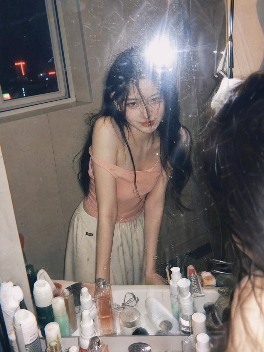jzaib4269's tweet photo. Created with GPT Image 2.0 on Yapper 

Prompt: Ultra-realistic candid film photography portrait of a young woman leaning over a bathroom sink and looking into a mirror at night, captured through a slightly dirty mirror with natural reflections and subtle imperfections. She has long black hair partially covering her face, soft glowing skin, and a gentle mysterious smile. Wearing a light pink off-shoulder fitted top and loose cream-colored lounge pants, she poses casually with both hands resting on the sink.
The scene is illuminated by direct on-camera flash, creating authentic Y2K disposable camera aesthetics, soft highlights, realistic skin texture, and natural shadows. A nighttime city skyline with colorful neon lights and high-rise buildings is visible through a nearby window, adding an urban atmosphere. The bathroom countertop is filled with skincare and cosmetic products, enhancing the lived-in, personal feel.
Shot from a close-up mirror perspective, cinematic composition, shallow depth of field, nostalgic 35mm film grain, subtle lens flare, reflections on glass, moody apartment ambiance, Korean lifestyle photography, intimate everyday moment, editorial fashion snapshot, raw candid energy, realistic colors, high detail, vertical composition, premium analog film aesthetic, trending Pinterest and Instagram photography style.