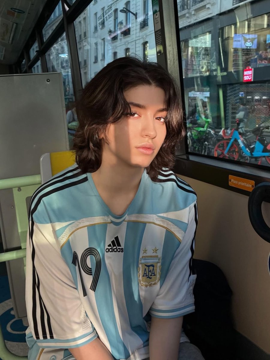 Sairah_0's tweet photo. GPT Image 2 On ChatGPT 

Prompt:

Ultra-realistic candid portrait of a young person with short wavy dark hair wearing an oversized Argentina national football jersey (#19), sitting on a city bus and at a bus stop during golden hour. Soft warm sunlight streams through large windows, creating dramatic light-and-shadow patterns across the face. Natural makeup, flawless pale skin, expressive eyes, relaxed confident expression, editorial street photography aesthetic. Urban European city background visible through the windows with bicycles, storefronts, and classic architecture. Shot on a 50mm lens, shallow depth of field, cinematic composition, authentic lifestyle fashion photography, highly detailed skin texture, natural colors, soft highlights, subtle film grain, Instagram editorial style, photorealistic, 8K, high dynamic range.

Negative Prompt:

blurry, low resolution, overexposed, oversaturated, extra limbs, distorted face, bad anatomy, unrealistic skin, heavy makeup, cartoon, CGI, watermark, text, logo artifacts, duplicate features, poor lighting, noise, cropped head, deformed hands.

Settings (optional):
•Aspect Ratio: 4:5
•Lens: 50mm f/1.8
•Lighting: Golden hour sunlight
•Style: Cinematic street photography, fashion editorial, photorealistic.