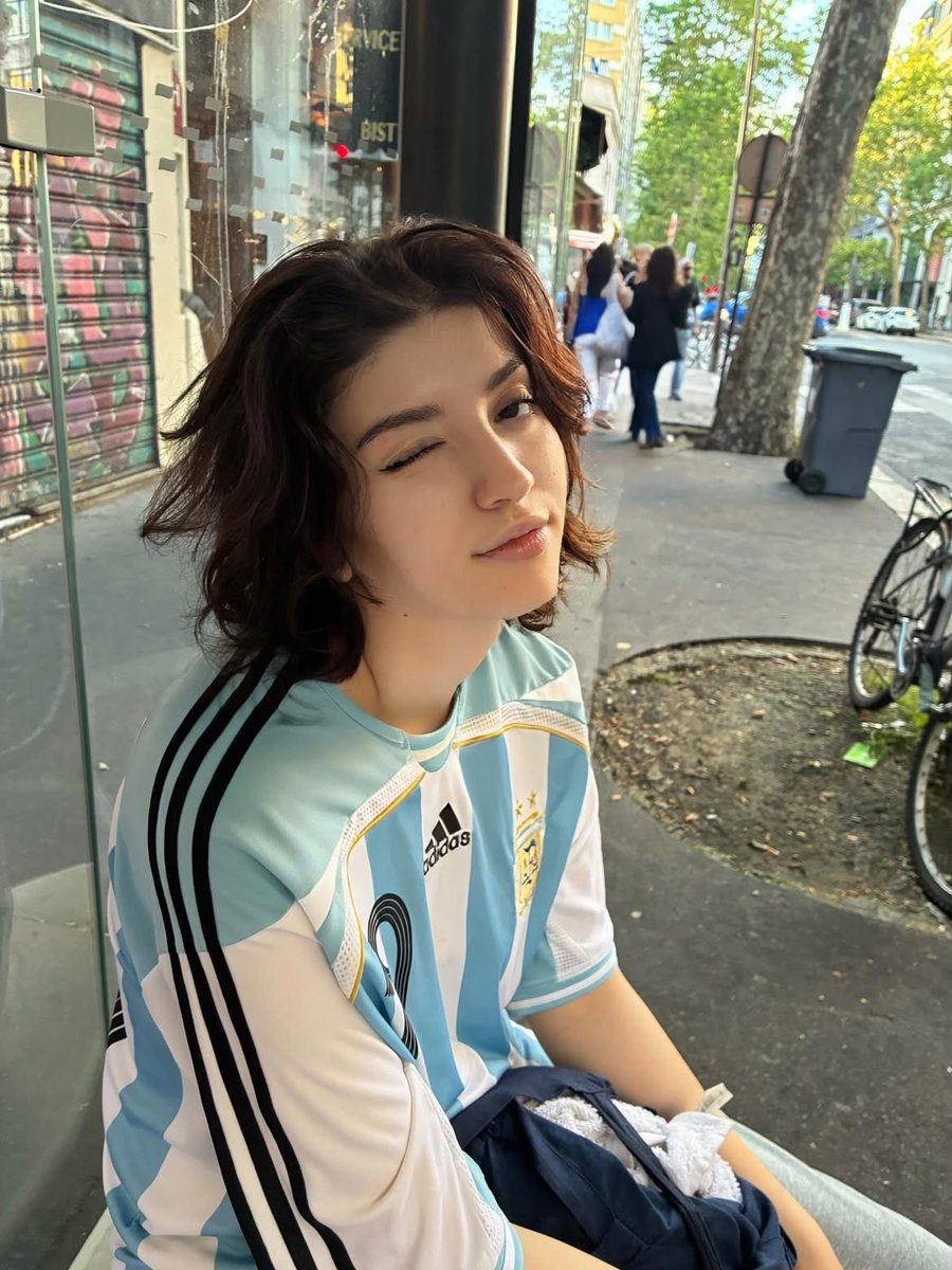 Sairah_0's tweet photo. GPT Image 2 On ChatGPT 

Prompt:

Ultra-realistic candid portrait of a young person with short wavy dark hair wearing an oversized Argentina national football jersey (#19), sitting on a city bus and at a bus stop during golden hour. Soft warm sunlight streams through large windows, creating dramatic light-and-shadow patterns across the face. Natural makeup, flawless pale skin, expressive eyes, relaxed confident expression, editorial street photography aesthetic. Urban European city background visible through the windows with bicycles, storefronts, and classic architecture. Shot on a 50mm lens, shallow depth of field, cinematic composition, authentic lifestyle fashion photography, highly detailed skin texture, natural colors, soft highlights, subtle film grain, Instagram editorial style, photorealistic, 8K, high dynamic range.

Negative Prompt:

blurry, low resolution, overexposed, oversaturated, extra limbs, distorted face, bad anatomy, unrealistic skin, heavy makeup, cartoon, CGI, watermark, text, logo artifacts, duplicate features, poor lighting, noise, cropped head, deformed hands.

Settings (optional):
•Aspect Ratio: 4:5
•Lens: 50mm f/1.8
•Lighting: Golden hour sunlight
•Style: Cinematic street photography, fashion editorial, photorealistic.