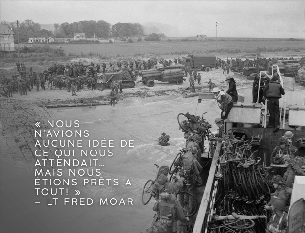 Photo en noir et blanc d’une embarcation de débarquement près du rivage, surchargée de bicyclettes et de soldats. Un grand nombre de soldats et quelques véhicules militaires se massent sur la plage. Texte sur l’image : « Nous n’avions aucune idée de ce qui nous attendait… mais nous étions prêts à tout! » – Lt Fred Moar