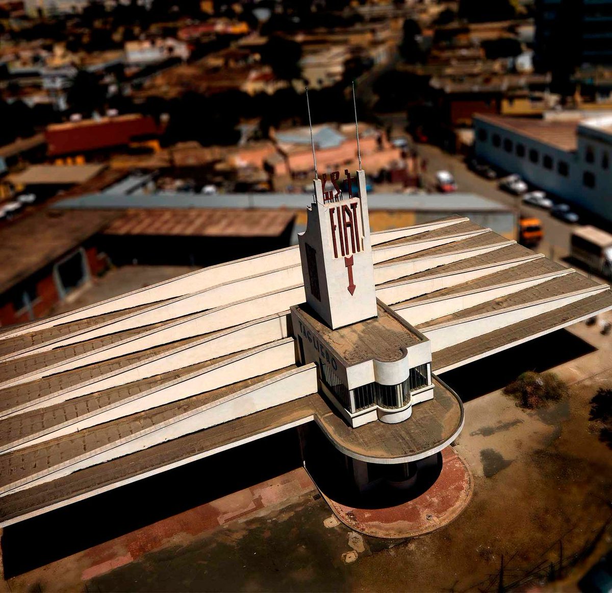 NestorSiurana's tweet photo. La capital de Eritrea fue diseñada por arquitectos italianos en los años 30.

Es la mayor concentración del mundo de arquitectura futurista y Art Déco, congelada en el tiempo.

Y sí, Asmara está reconocida oficialmente por la UNESCO como Patrimonio de la Humanidad.

Durante la ocupación colonial italiana, el dictador Benito Mussolini quiso transformar la pequeña ciudad en una metrópoli de vanguardia que sirviera como vitrina del fascismo en África.

Al estar lejos de las estrictas normativas urbanísticas de Europa, los arquitectos italianos utilizaron Asmara como un laboratorio experimental para plasmar las ideas más radicales de la época.

Especialmente entre 1935 y 1941, se levantaron miles de edificios con líneas aerodinámicas, ventanas de buey y formas geométricas audaces.

El Fiat Tagliero (1938), es la obra cumbre del futurismo arquitectónico.

Diseñada por Giuseppe Pettazzi, es una estación de servicio con la forma de un avión de pasajeros y espectaculares alas de hormigón voladizas que se sostienen sin pilares.

El Cinema Impero (1937), también es el máximo exponente del Art Déco en la ciudad.

Destaca por su imponente fachada vertical, sus motivos geométricos y los portones de cristal inspirados en circuitos eléctricos.

Bar Zilli y otros comercios también son edificios que simulan la forma de un aparato de radio antiguo, villas residenciales cubistas y hoteles con interiores idénticos a los de la década de 1930.

¿Pero por qué se congeló en el tiempo?

La ciudad sobrevivió intacta debido a décadas de aislamiento político y a un largo conflicto de independencia con Etiopía.

La falta de recursos económicos impidió el desarrollo inmobiliario moderno, protegiendo sin querer todo el casco histórico de la demolición y preservando el entorno urbano tal como lo dejaron los italianos en 1941.