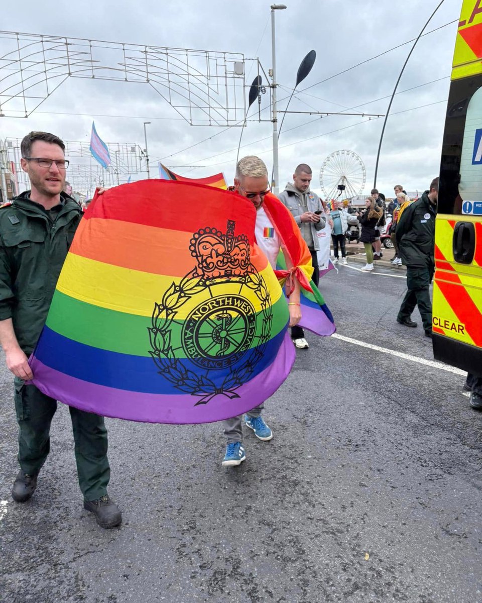 Two colleagues walk beside an ambulance carrying a rainbow NWAS Pride flag during the Blackpool Pride parade.