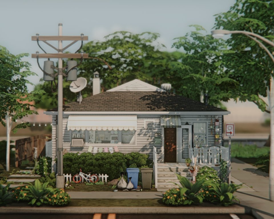 A front view of a NoCC (CC-free) single-story house in The Sims 4, featuring vintage striped window awnings and a dark wood front door. This house is inspired by a real-life home.