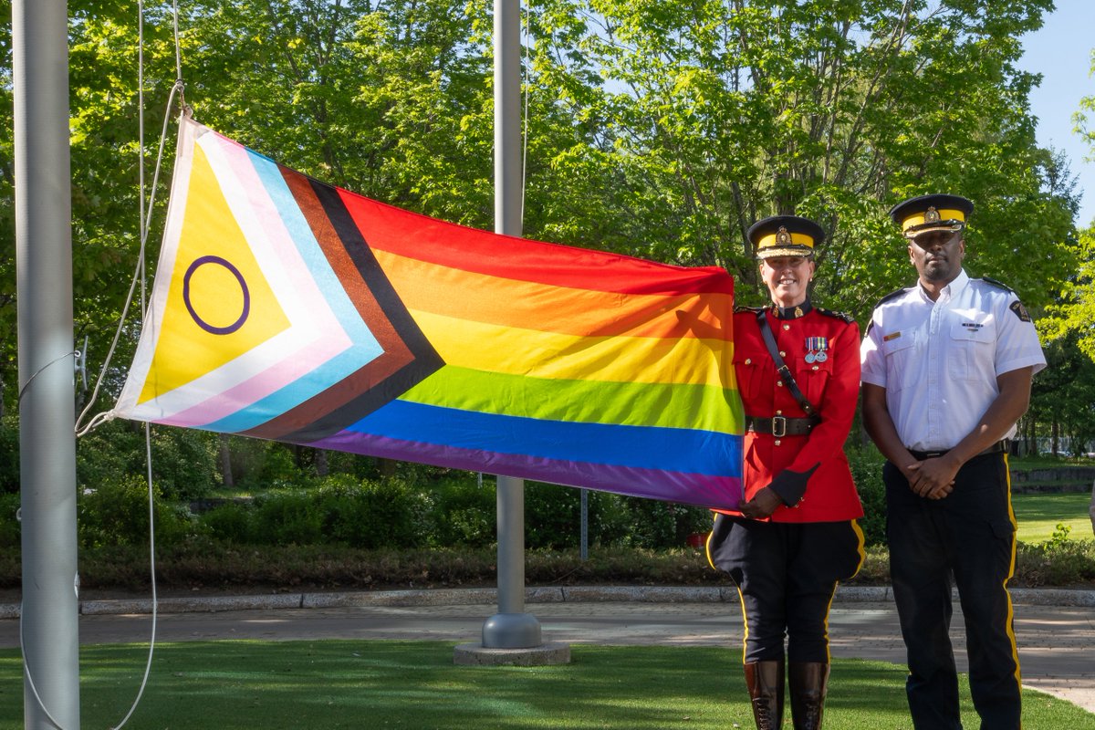 Two RCMP members stand beside the Pride flag during the Pride Flag raising ceremony marking the start of Pride Month.