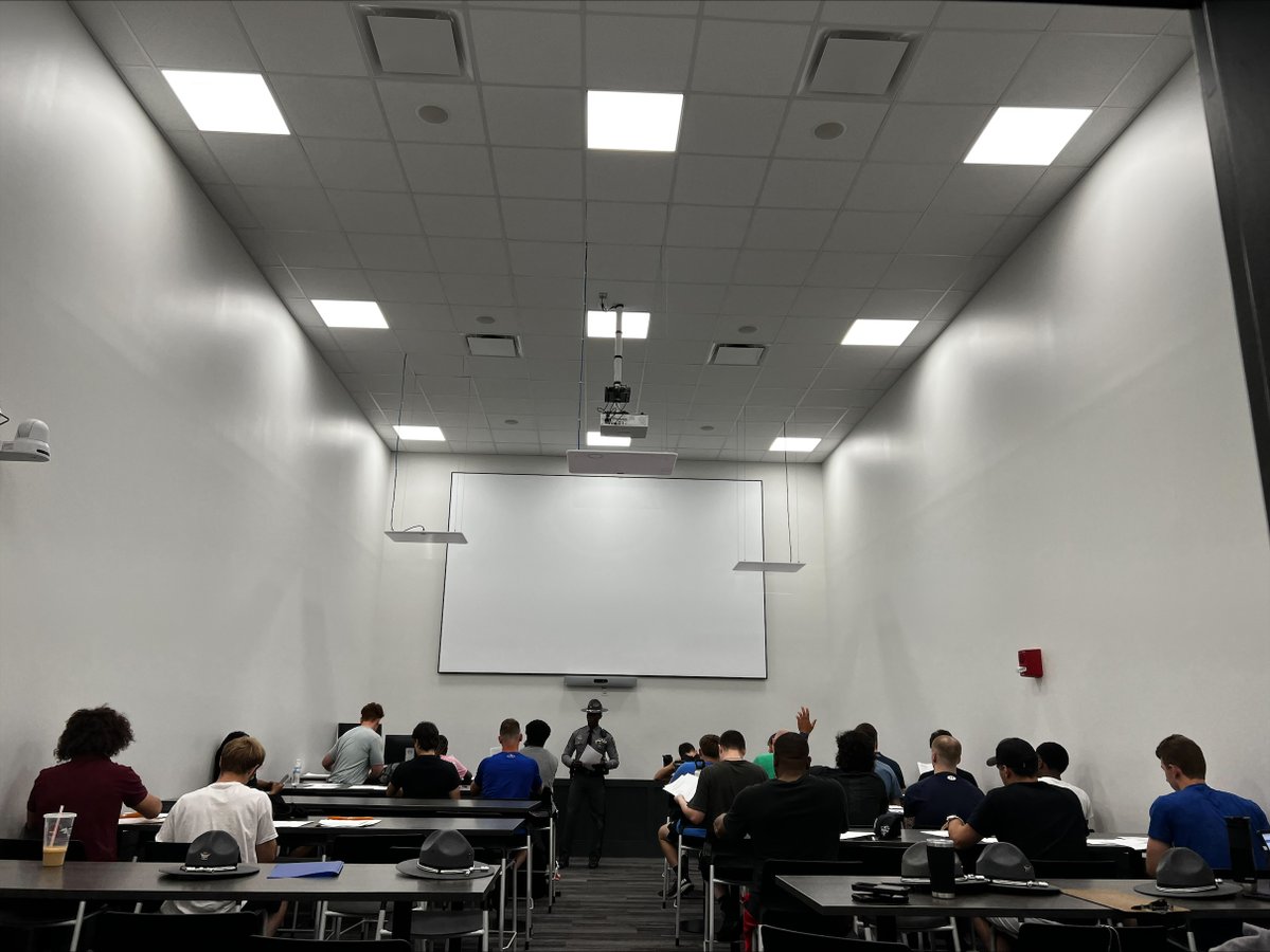 A trooper is speaking in front of a classroom with more than 15 potential applicants. 