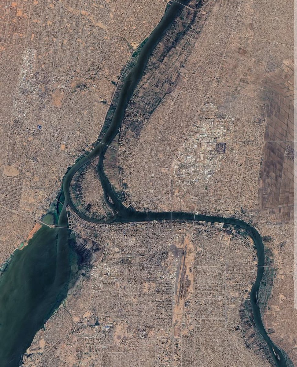 NestorSiurana's tweet photo. Hay lugares en el mundo donde la geografía modela las ciudades.

Jartum, la imponente capital de Sudán, es el ejemplo definitivo.

Nace en el punto exacto en el que el Nilo Blanco y el Nilo Azul se unen tras un viaje de miles de kilómetros.

En Jartum, empieza el Nilo que conocemos todos.

Esta metrópolis se levanta como un colosal puente entre el Mundo Árabe y el corazón del África Subsahariana.

Es una urbe de contrastes brutales, donde la inmensidad del paisaje desértico choca con un bullicio humano que desafía constantemente a la historia.

Es una capital tripartita.

Jartum no es una ciudad común; es, en realidad, un organismo vivo compuesto por tres almas distintas separadas por las aguas del río. Se la conoce popularmente como la capital triangular.

El área metropolitana está integrada por:

1. Jartum, el centro administrativo y político, originalmente diseñado con un trazado de grandes avenidas arboladas.

2. Omdurmán, en la orilla occidental, el núcleo histórico, espiritual y tradicional del país.

3. Jartum Norte (Bahri), la zona industrial y el motor comercial de la región.

Esta gigantesca conurbación se despliega sobre miles de kilómetros cuadrados.

Su fisonomía horizontal está marcada por calles anchas y un crecimiento que parece estirarse infinitamente hacia las tierras áridas que la rodean.

En su mismísimo centro geométrico flota la isla de Tutti, un reducto de cultivos tradicionales y manglares que sobrevive como un oasis verde rodeado de puentes modernos y asfalto.

La escala humana de Jartum es masiva y de una juventud vibrante.

El área metropolitana del Gran Jartum alberga a más de 8 millones de habitantes, lo que la consolida como una de las aglomeraciones urbanas más pobladas y de más rápido crecimiento de todo el continente africano.

Esta explosión demográfica es el reflejo de un país que funciona como un crisol absoluto.

La población de la urbe es un reflejo directo del éxodo rural y del desplazamiento interno provocado por las vicisitudes políticas y climáticas de la región.

El resultado es una sociedad con una edad media notablemente joven, inferior a los 19 años, llena de energía, resiliencia y una profunda riqueza cultural que se manifiesta en sus mercados, su música y su mística sufí.

Pasear por el tejido urbano de Jartum equivale a leer las páginas de su compleja historia a través de sus fachadas.

Su patrimonio arquitectónico es una fascinante mezcla de estilos coloniales, tradicionales y vanguardistas.

El estilo de Jartum está desarrollado con fuerza durante la segunda mitad del siglo XX, esta corriente mezcló la simplicidad del racionalismo moderno con soluciones ambientales adaptadas al calor extremo del desierto.

La huella otomana y colonial está muy presente.

En el corazón de la capital destaca la Gran Mezquita de Jartum, construida a principios del siglo XX con una marcada estética otomana.

Cerca de allí, antiguos edificios gubernamentales recuerdan la época del condominio anglo-egipcio, definidos por arcadas de ladrillo rojo y amplios pasillos ventilados.

La tradición de Omdurmán también es increíble.

En claro contraste con la planificación europea de Jartum, Omdurmán preserva un diseño orgánico de callejuelas estrechas, mercados de adobe y monumentos históricos fundamentales como la tumba del líder nativo Muhammad Ahmad (el Mahdi).

Durante las últimas décadas, la inyección de capitales extranjeros transformó el horizonte de la ciudad a la orilla del río, levantando rascacielos de cristal, hoteles de lujo con forma de vela y puentes de ingeniería avanzada que enlazan las tres bandas de la metrópolis.

A pesar de las severas crisis políticas y los conflictos armados que trágicamente han golpeado y transformado la capital en los últimos años, Jartum conserva una identidad inquebrantable.