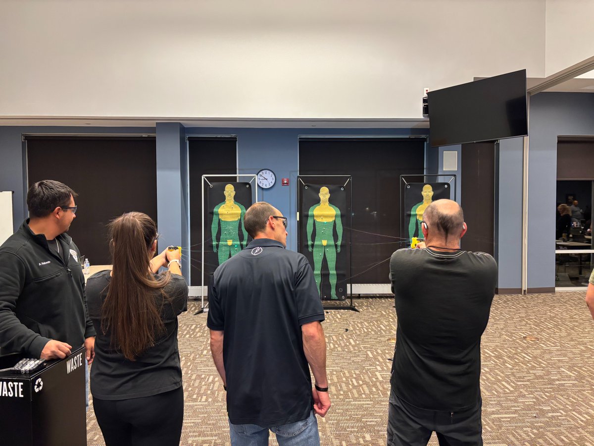 Two instructors standing with two participants aiming a taser at three practice targets.