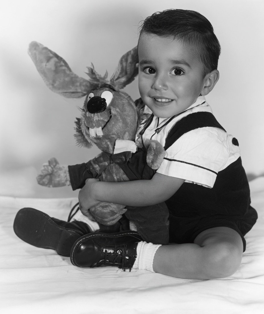 FLCons's tweet photo. This young man would soon be trading in his bunny for his first musical instrument.  At age 6 he dabbled with an accordion, but by age 12 and because of influences like Hendrix and other guitar gods of the day, he picked up his first guitar.  

Self taught, he pointed to many influences such as Duane Allman and Johnny Winter because of their phrasing and musical vocal like solos.

I rate this man as one of my top most favorite guitar players ever.   Do you know who he is?

Btw - I sharpened this image up with grok.