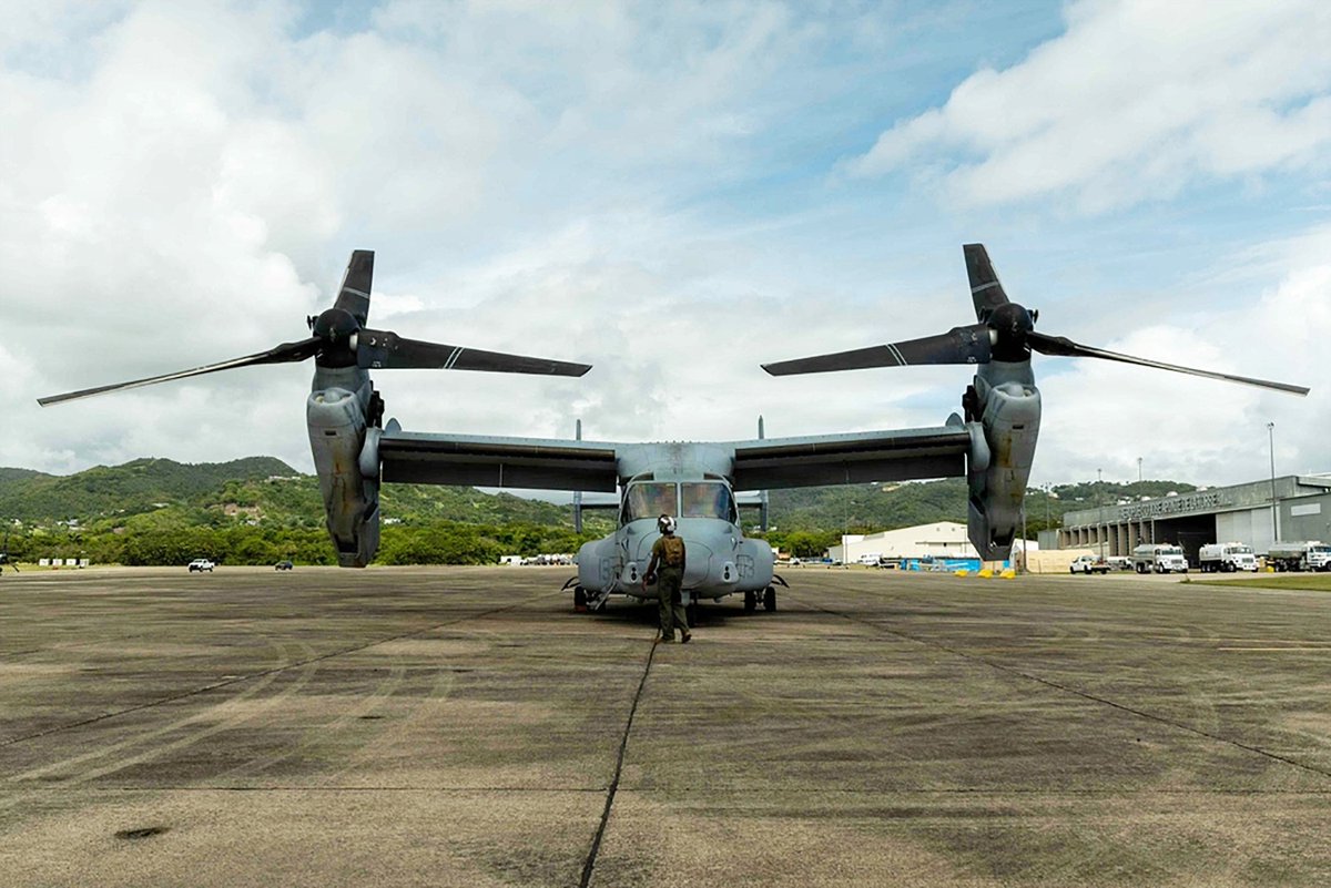 A Marine stands beneath a MV-22B Osprey as the aircraft prepares for operations on an airfield in the Caribbean.