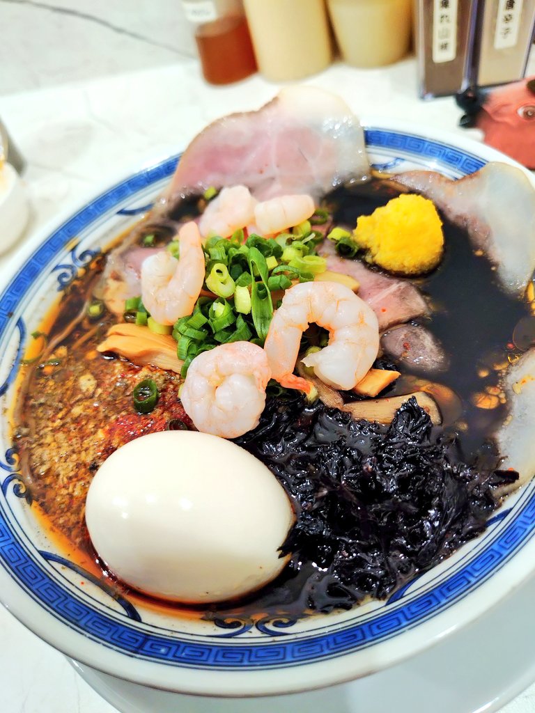onipuka's tweet photo. 【無冠】
🚉阿佐ヶ谷
🍜阿佐ヶ谷BLACK（辛アヒージョ）蕎麦粉入り麺

ルージュ差す
ノアールの海に
オイスタ���
六月の夜を
深くしてゆく

な件🌹🖤🦪

今日は阿佐ヶ谷BLACK（辛アヒージョ）！

丼着！🍜

テーブルに備えられた紙エプロン！

嬉しいサービスですが���は着用しません🐴

こちとらカレーうどんだって
跳ねた事ないっーつの！😤

目の前に現れた丼は
まさにノアールの海🌊🖤

ルージュの赤が映えて
なんとも妖艶なビジュアル✨

まずはスープをひと口

牡蠣の旨味がドン！🦪🔥

そこへ辛アヒージョの香りと刺激が重なり
パンチの効いた仕上がりです🐴

蕎麦粉入りの麺も
チュルチュルと心地良く
黒いスープをしっかり纏ってくれます🍜✨

後半になるほど
牡蠣の旨味と辛味が重なって加速！

ズルズル啜っていたその時…

あひゃー！！💥

黒い染みついてもうた😭😭😭

女性の皆様は素直に紙エプロン着けましょう🥲

そんなこんなで
しっかり完飲完食でした🐴🖤

この度も美味しく頂きましたご馳走様でした🐴