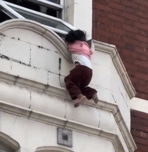 IlmFeed's tweet photo. A hero who saved a girl after she fell from a window ledge in East London has been identified as Mohamed Jesil.

In a video shared on social media, the girl can be seen hanging from a window ledge while members of the public gather below.

Moments later, a police officer and Mohamed position themselves beneath her in an attempt to help.

Mohamed was getting ready for work when he heard the commotion and rushed outside to help, still shirtless.

What followed were a few tense moments as onlookers watched anxiously. Suddenly, the girl lost her grip and fell, but Mohamed managed to catch her and take her to safety.