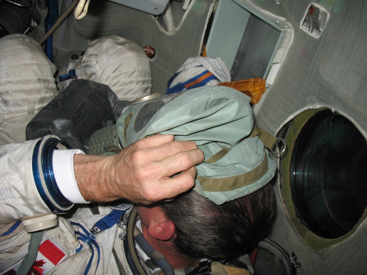 Cmdr_Hadfield's tweet photo. Putting on a spacesuit while wearing a gas mask. 
If we have a spaceship fire, we rapidly don oxygen masks for the smoke. The tricky part is then getting into the spacesuit without breathing noxious fumes - need to hold your breath for a while. 
These photos are from a training session in the Star City simulator. Once we learn how, we do it again with the cockpit filled with smoke. 
A good skill to have confidence in.