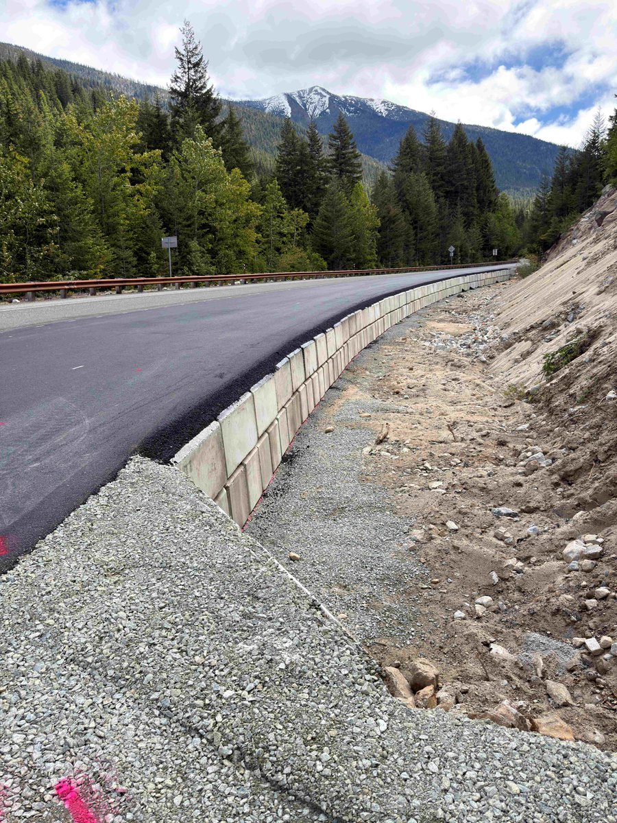 A fresh stretch of asphalt, shoulder rock and a concrete block wall along a mountainous stretch of State Route 20/North Cascades Highway.