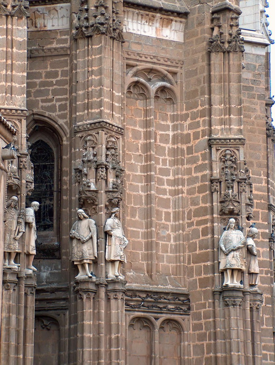trastamara_ana's tweet photo. Elevados sobre los contrafuertes de la cabecera del monasterio de San Juan de los Reyes, doce personajes sostienen escudos y contemplan la ciudad desde hace más de quinientos años.

Son heraldos reales. En tiempos de los #ReyesCatólicos, estos oficiales llamados también "reyes de armas" eran figuras fundamentales en el protocolo cortesano. 

Encargados de preceder a los monarcas en sus actos públicos, proclamaban sus decretos y presentaban sus mensajes oficiales en las cortes de otros reinos. 
Pero, además, su número encierra un mensaje: doce era el número de los apóstoles. La corte terrenal encontraba así su reflejo en el orden celestial.

Doce era también una imagen de totalidad. Los heraldos representaban una autoridad capaz de alcanzar todos los territorios de la Corona, llevando la ley, el linaje y la palabra real en todas las direcciones.

Y existe una tercera lectura aún más profunda: reino y fe forman parte de una misma arquitectura simbólica.
Por eso los heraldos custodian el monasterio, porque San Juan de los Reyes fue concebido como una Iglesia y también como una idea de España tallada en piedra.
#Toledo
#ReyesCatólicos