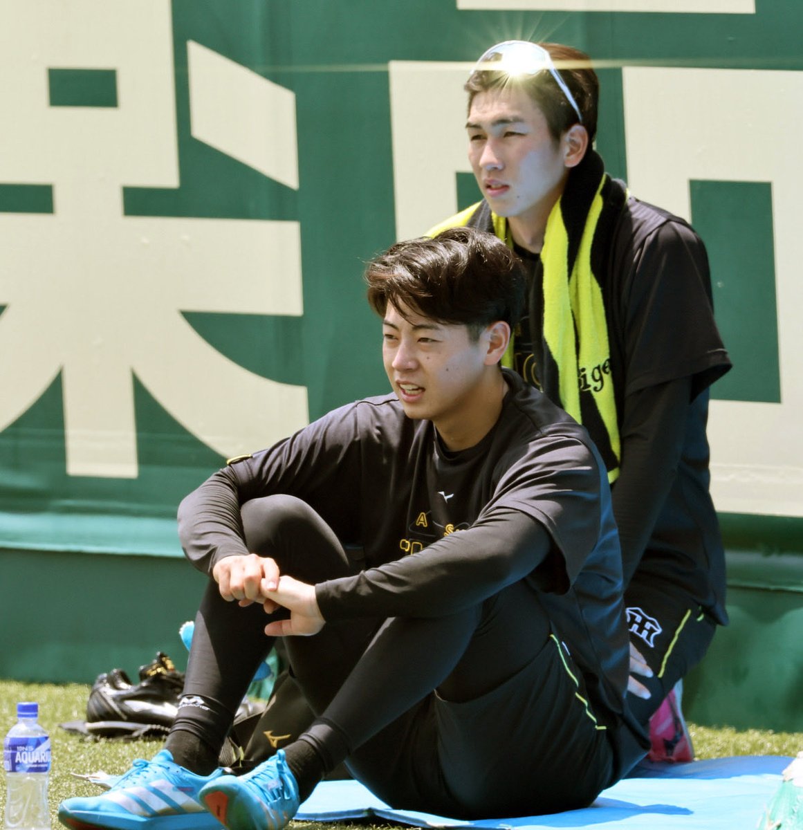 dailytigers2026's tweet photo. デビュー戦を控える下村投手。練習中からいい表情です。後ろに座る今朝丸投手のサングラスがキラッと光っています🤩 https://t.co/vhZwmGGow2