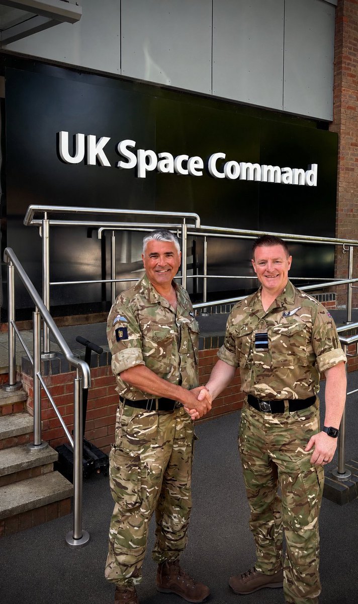 Major General Paul Tedman and Air Vice-Marshal Jamie Thompson shake hands in front of the UK Space Command building. 
