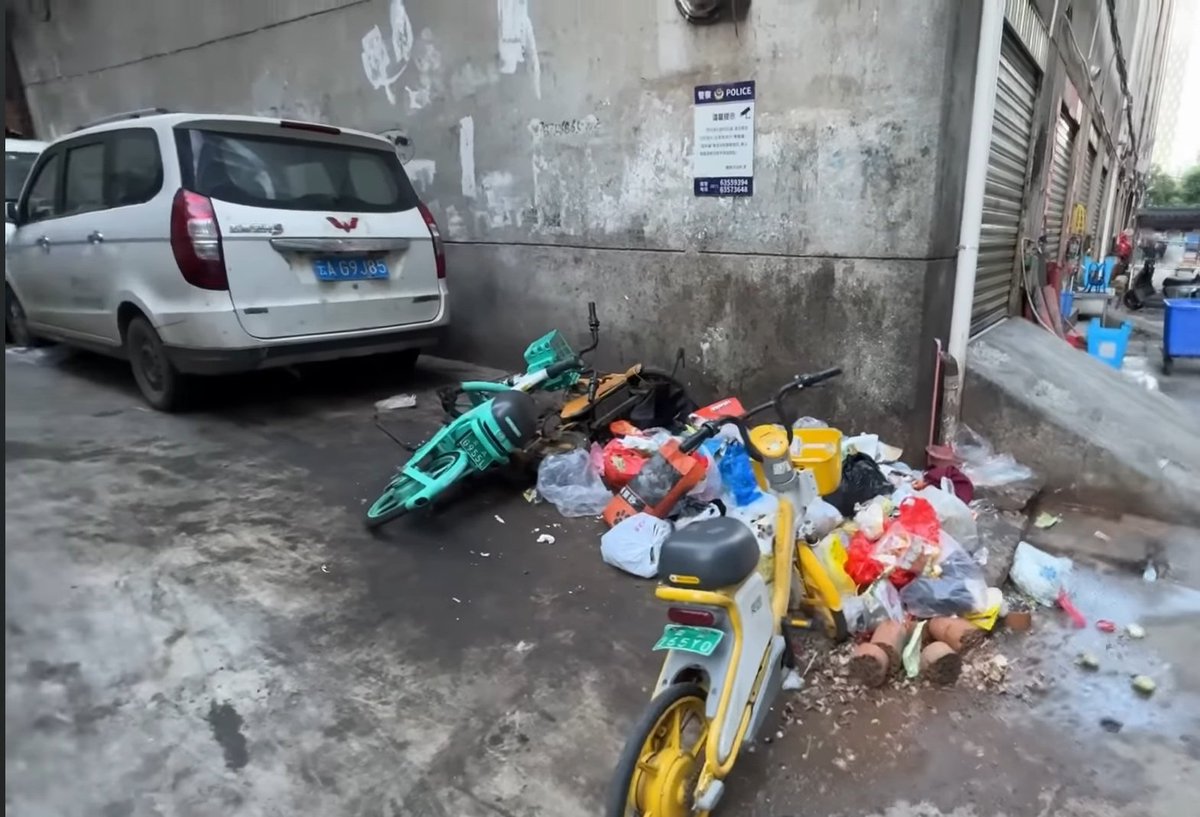 Wellutwt's tweet photo. Vendor making food with bare hands, ingredients stored on the ground near a gutter, and a dirty street all around. 
This is a Lower Caste Shang Neighbourhood in the Capital Region of China. 🤢 https://t.co/oPOrZ41bim