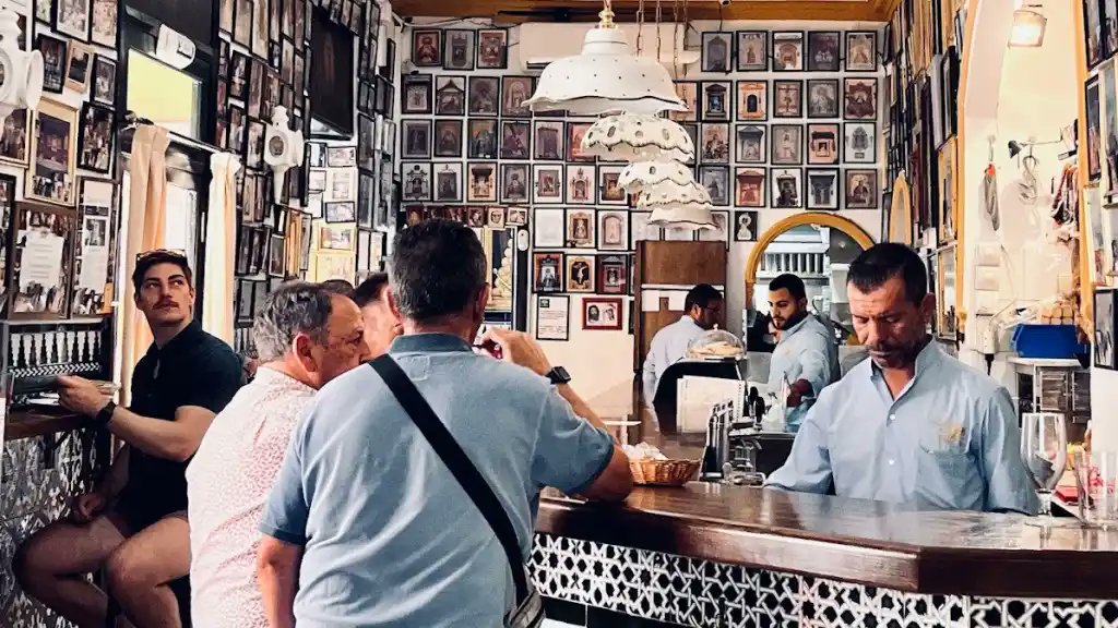 PROMAKOS_'s tweet photo. ¿Cuándo cambió España el vino por la cerveza? La historia cotidiana de un vuelco, del vino de la taberna a la cerveza del bar. (Hilo)

Entras hoy en cualquier bar de España, pides una caña sin pensarlo y a nadie le extraña, porque la cerveza es ya la bebida que se sirve por defecto en la barra. Y eso en uno de los grandes países vinícolas del mundo, en la tierra de la Rioja y el Jerez, donde durante siglos se bebió vino como quien bebe agua, es una rareza con su historia interesante y el cambio es mucho más reciente de lo que parece y no ocurrió por las razones que uno imaginaría.

Cuando el vino era alimento

Hasta bien entrado el siglo XX, el español medio bebía vino a diario y en cantidades que hoy asustarían a cualquier médico. Las series que han reconstruido los historiadores económicos del vino, con Vicente Pinilla y Eva Fernández a la cabeza, sitúan el consumo en torno a los noventa y cinco litros por habitante y año a comienzos de siglo, esto es, más de un cuarto de litro diario por cabeza contando a niños, ancianos y abstemios. El vino era allí, mucho más que un placer de sobremesa, el combustible barato del jornalero y del campesino, un alimento que aportaba calorías a quien las quemaba en el campo y que acompañaba al pan en la mesa de las clases populares. Su templo era la taberna, centro de la vida del barrio y del pueblo, donde se fiaba el trago y se mataba el rato.

Aquel vino, eso sí, poco tenía que ver con el que hoy llena las copas de las denominaciones de prestigio. Era vino ordinario, comprado casi siempre a granel, pues todavía en 1968 el sesenta por ciento se vendía sin embotellar, de mucho grado y poca finura, y cerca del cuarenta por ciento de las familias lo rebajaba para poder beberlo a diario sin caer redondo. España bebía mucho vino, pero malo, y a diferencia de Francia no hizo a tiempo la apuesta por la calidad. La historiadora Eva Fernández ha estudiado el fenómeno: a finales de los años ochenta apenas uno de cada seis litros consumidos en España era vino fino, una proporción que los franceses habían alcanzado quince años antes. Bebíamos como una potencia vinícola y, a la vez, como un país que despreciaba su propio vino.

De la taberna al bar

La cerveza, mientras tanto, era cosa de minorías. Todavía hacia 1959, en una ciudad como Madrid, el vino acaparaba el setenta por ciento de la bebida que se consumía y la cerveza apenas un veintisiete. Lo que dio la vuelta al panorama fue el desarrollismo de los años sesenta, aquella década de éxodo del campo a la ciudad, con fábricas nuevas y televisores encendidos en algunos hogares. El historiador Alonso Moreno, que ha estudiado el sector cervecero español por dentro, a partir de las actas de una vieja fábrica jienense, resume el vuelco en una fórmula afortunada: el paso de la taberna al bar, del mundo rural al urbano, y con él del vino a la cerveza. Las cifras de producción acompañan la sentencia, pues la cerveza fabricada en España se multiplicó casi por cuatro en aquella década, de tres millones y medio de hectolitros en 1960 a más de doce millones en 1970, mientras en el resto de Europa crecía apenas un tercio.

Pesó también el turismo. Los millones de visitantes del norte de Europa que llenaron las playas a partir de los sesenta, bajo el reclamo de aquel 'Spain is different', eran bebedores de cerveza, y su gusto se contagió a un país que empezaba a mirar lo extranjero como sinónimo de lo moderno. La cerveza se vistió de cosa joven, urbana y nueva, mientras el vino a granel quedaba arrinconado del lado de lo viejo y lo campesino. Ayudó también el clima, pues una caña fría y ligera apetece bajo el sol de agosto más que un tinto denso de catorce grados. El formato hizo el resto, con la litrona, popularizada desde Barcelona, metiendo la cerveza en una casa que hasta entonces solo la conocía de la barra del bar. Y por encima de todo estuvo la publicidad, que halló en la televisión recién llegada su gran altavoz.⬇️⬇️