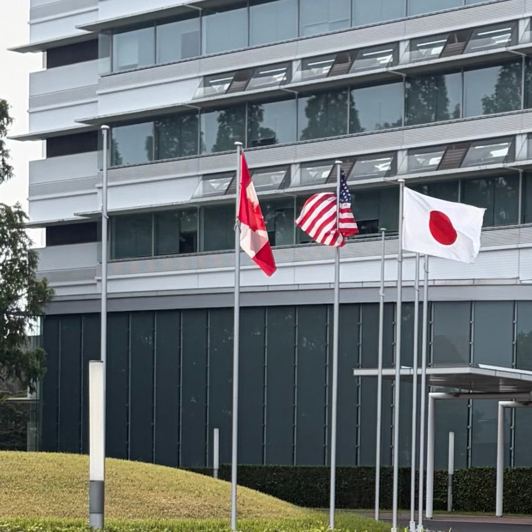 Un immeuble de bureaux avec les drapeaux du Canada, des États-Unis et du Japon flottant devant.
