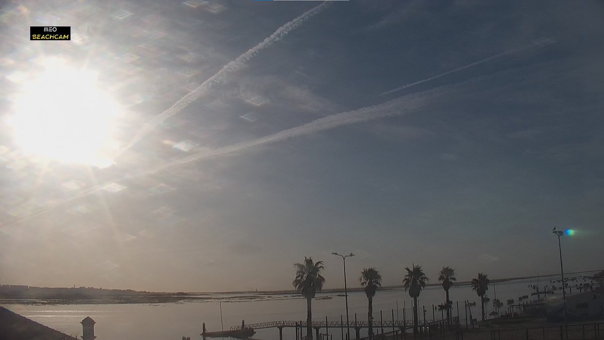75Alcaide's tweet photo. 18/06/2026 07:50: O CÉU DE FARO CORTADO ÀS TRÊS PANCADAS NESTA MANHÃ.🛩️🤕

Bom dia a todos,

A imagem da Beachcam de Faro expõe o esqueleto do espetro: traços lineares massivos cruzam-se mesmo em frente ao Sol.
A dispersão expande-se e cria um manto pastoso que apaga o azul natural do céu.
Está horrível.

Esta névoa persistente e leitosa atua como uma autêntica lente difusora (RIS).

Enquanto as partículas assentam na inversão térmica, preparam o cenário para as calibrações de radares pesados e satélites do padrão #IMT2030 (6G).

Entretanto as quebras na rede elétrica sucedem-se, queimam equipamentos, provocam incêndios mas ninguém fala disto.

Algo me diz que este dia vai longo.

#Faro #Algarve #Meteorologia #OSINT #Portugal #FiedlLab #LivingLab