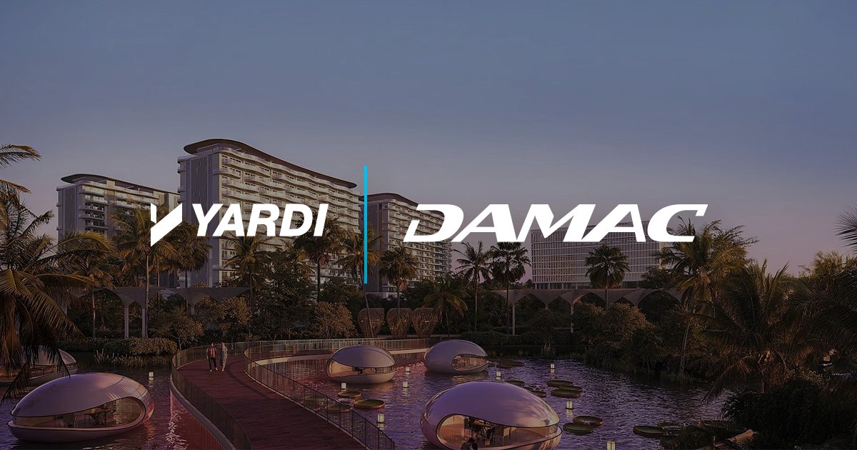 A scenic view features a large pond with decorative globe lights and a wooden walkway. In the background, modern buildings are visible surrounded by palm trees. The logos of "Yardi" and "Damac" are prominently displayed in the sky above the scene.