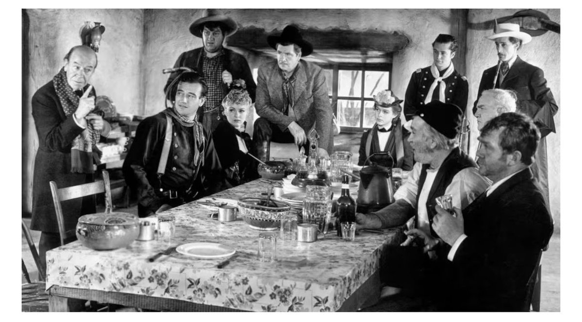 fordianos's tweet photo. John Ford es un genio en la utilización del plano fijo general, lo hace para apoyar el guión.

El plano fijo de la cena en Stagecoach es una clase magistral de composición dramática. Al sentar a Dallas (la prostituta) y a Ringo (el fugitivo) a un lado, alejados del resto de los pasajeros "respetables", Ford utiliza la profundidad de campo y el espacio vacío entre los personajes para reflejar el guion a la perfección: el puritanismo y el severo clasismo de la sociedad frente a los marginados. 
Todas esas ideas las desarrolla de manera visual, sin palabras, herencia de su bagaje en el Hollywood silente.
En esa parada en la estación de Apache Wells se produce el plano fijo donde los personajes de Dallas y Ringo Kid quedan arrinconados a un lado de la mesa, mientras los pasajeros de "clase alta" los miran con desprecio y se distancian físicamente de ellos.
La narrativa visual uno de los factores diferenciales en la obra de John Ford.#fordianos