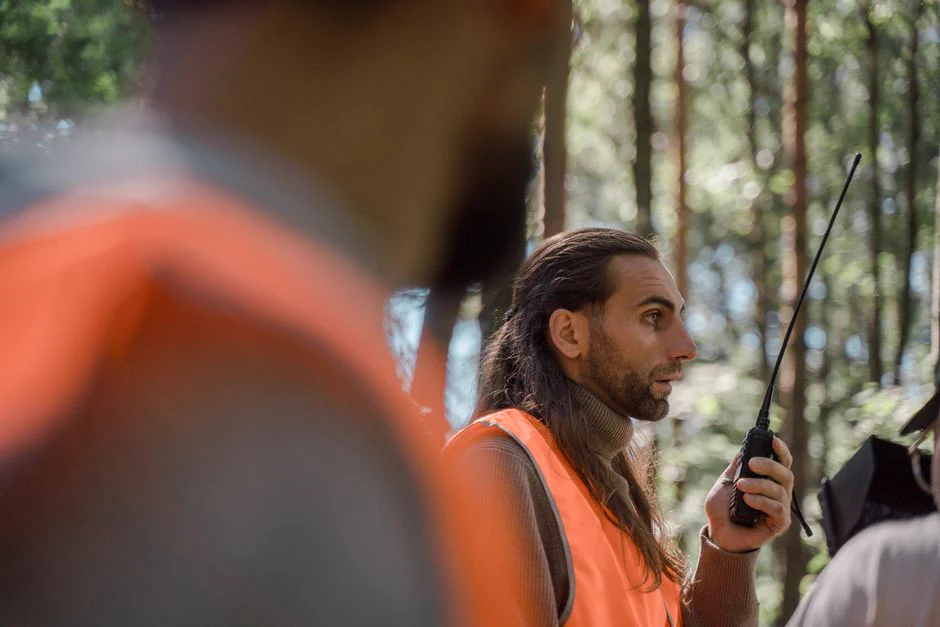 Men in high-visibility vests communicate using walkie-talkies in a forest setting. Public domain.