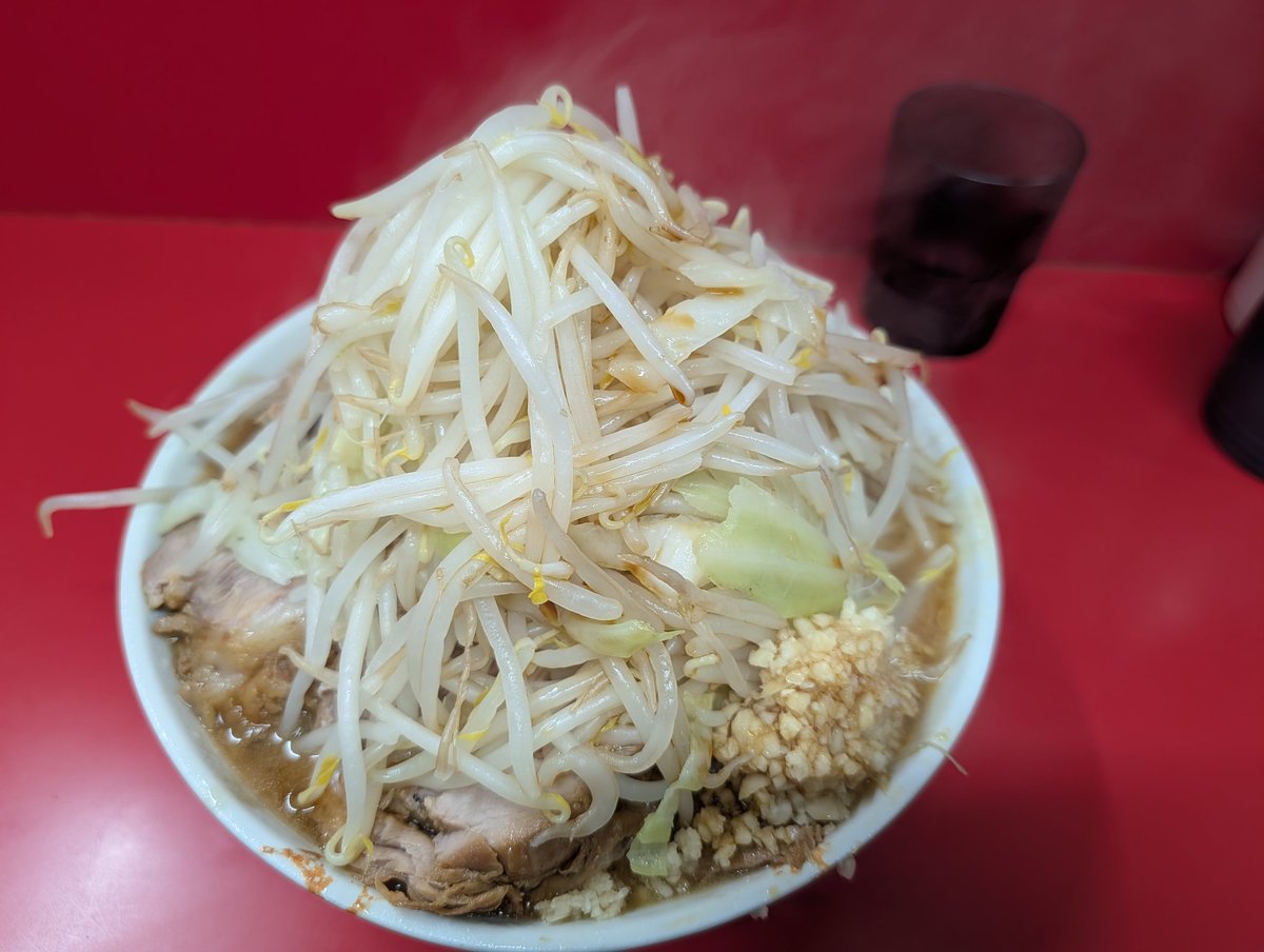 JOJI0529's tweet photo. 今日は単発で小平の現場だったので仕事帰りに久しぶりにラーメン二郎一橋学園店まで行ってきました。自分調べでは2024年3月以来なので2年3か月ぶりです。

17時15分位に店に到着すると先客は6人程でそこまで並んでなかったです。17時半に店がオープンし食券を購入し店内へ。ギリギリファーストロットに間に合わずセカンドロットになり17時55分着丼。コールはいつも通りヤサイカラメニンニクだ。

山盛りのヤサイに巨大なブタが2枚、大量の刻みニンニクは正にラーメン二郎そのもの。小で推定麺量400gだからかなり多い。流石神田神保町店で修行した店主だけある。値上げしても量は減らさないこの姿勢は個人的には大歓迎、量が多くてこそのラーメン二郎だからだ。

仕事帰りということもあり腹が減っていたので10分程で完食。久しぶりの一橋学園二郎は腹一杯で大満足です！ごちそう様でした！