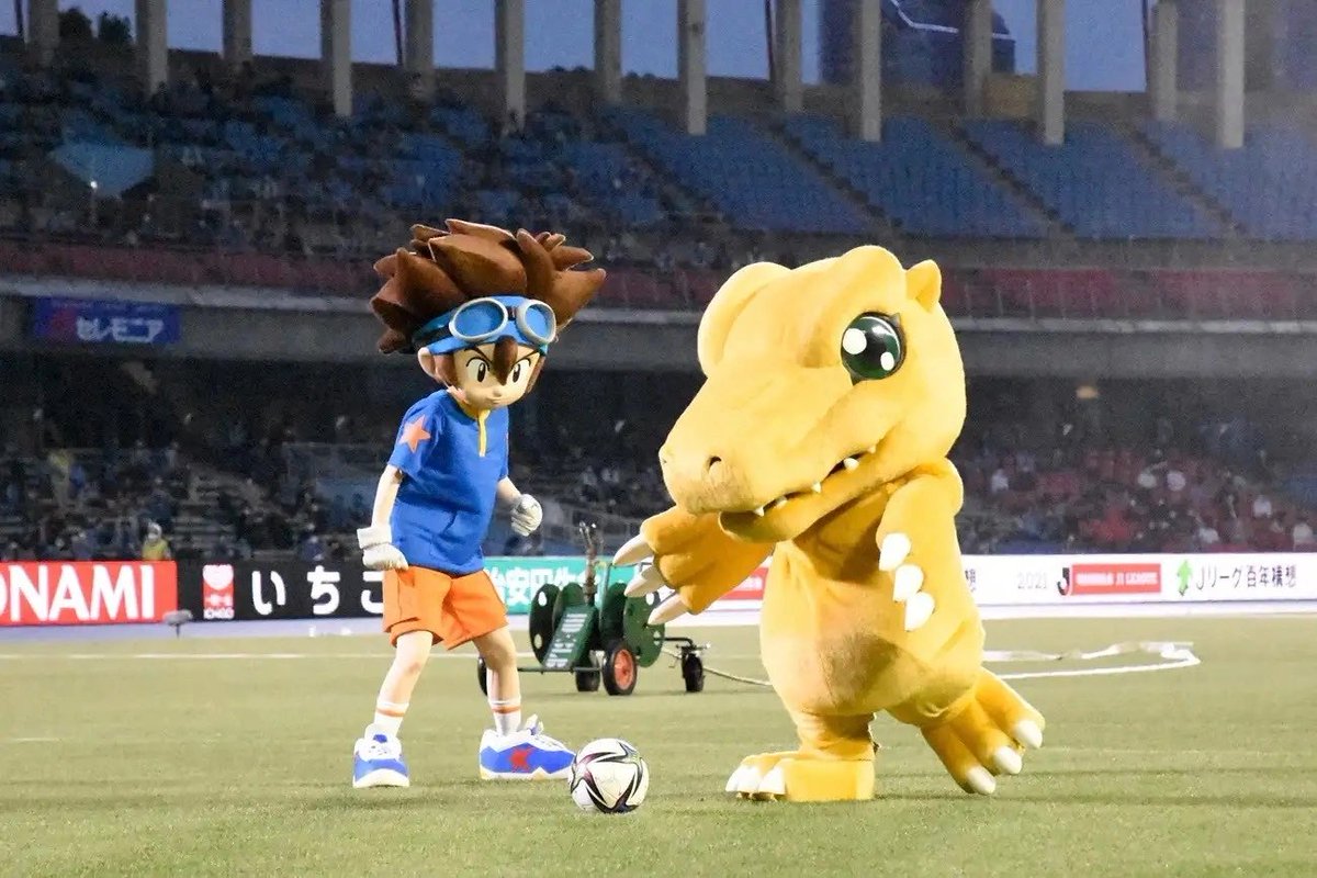 SailorV148's tweet photo. Flashback to May 2021, when Taichi and Agumon took over the pitch for a special J-League collab! Representing Kawasaki City, which is the real-world setting for Digimon Adventure: (2020), Agumon delivered the opening kick of the match between Kawasaki Frontale and Kashima Antlers.

Call it the power of "Crest of Courage," but that single game ended up breaking ultimate J-League records. Kawasaki Frontale won 2-1, locking in a historic 20-game winning streak from the start of the season. To top it off, their manager, Toru Oniki, became the fastest manager in league history to hit 100 wins!

#digimon #digimonadventure #デジモンアドベンチャー