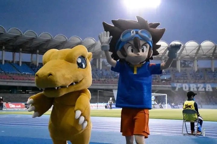 SailorV148's tweet photo. Flashback to May 2021, when Taichi and Agumon took over the pitch for a special J-League collab! Representing Kawasaki City, which is the real-world setting for Digimon Adventure: (2020), Agumon delivered the opening kick of the match between Kawasaki Frontale and Kashima Antlers.

Call it the power of "Crest of Courage," but that single game ended up breaking ultimate J-League records. Kawasaki Frontale won 2-1, locking in a historic 20-game winning streak from the start of the season. To top it off, their manager, Toru Oniki, became the fastest manager in league history to hit 100 wins!

#digimon #digimonadventure #デジモンアドベンチャー
