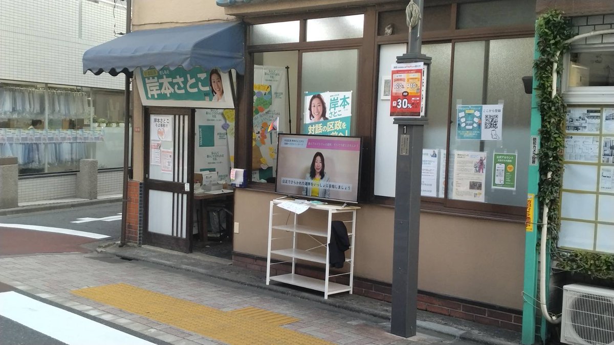 HirokoKado's tweet photo. 岸本杉並区長の西荻の新事務所の前のモニターが、公選法違反なのではないか？とうちの事務所にご意見や写真が送られてきました。
私からすれば、黒に近いグレーぽい、仮に黒でも形式犯ぽいですが、その辺の判断は当局の手に委ねられます。
岸本区長が、公職なのに法令ギリギリ（てかアウト？）、脱法行為というのはなかなかのストロングスタイルだなという感想です。

以下、私の理解です。

【岸本区長事務所前の公道に向けて外に設置した大型モニターは公選法違反か？】

① 公選法上、（選挙期間ではない）政治活動期間では、候補者等の氏名・氏名類推事項（顔写真・似顔絵等）を表示する文書図画の掲示には一定の制限がある。（政党等の政治活動を除きます。岸本区長は無所属と自称）
② モニター等によって表示されるものは、形態上はデジタルサイネージ（電子看板）と同様であり、公選法では看板類（立札・看板の類）と見なされる。動画もありますが、ずっと岸本区長の顔が出てる状態。
③ ①に制限されない②の看板類は、候補者等または後援団体の政治活動のために使用されるものに限定され（公選法143条16項1号）、実質的にそれは政治活動用事務所看板とされる。
④ ③の看板は1基が150×40cm以内のサイズ制限、候補者等・後援団体で各6枚ずつの枚数制限がある他、区市選管に証票の交付申請をし、その証票の貼付がない看板は掲示禁止となる。（公選法143条17項）

よって、岸本区長の氏名・氏名類推事項を表示するモニターは③の政治活動用事務所看板と見なされるが、④のサイズ制限オーバーの上、証票の貼付が認められないように見えることから、そもそも掲示できない看板類と指摘されうる。
（※なお、軒下の横型の事務所看板には証票が貼ってあります）