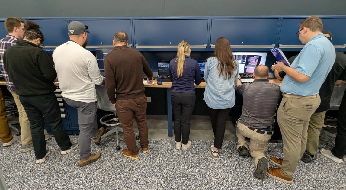 Eight Students standing next to each other in front of computers taking part in a training at the FBI Kinetic Cyber Range in Huntsville, Alabama.