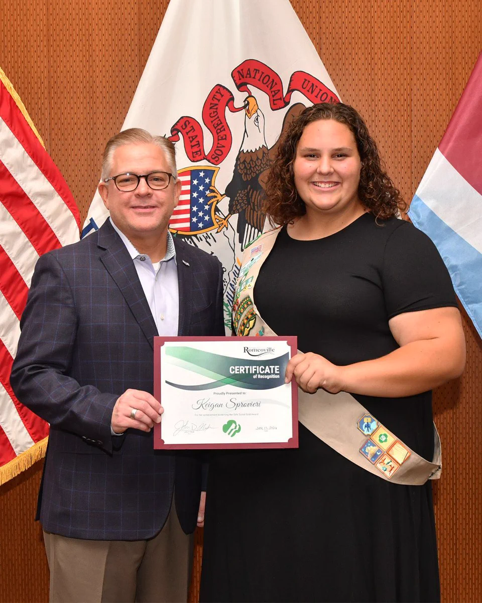 A man and a woman stand in front of flags while holding a piece of paper. 