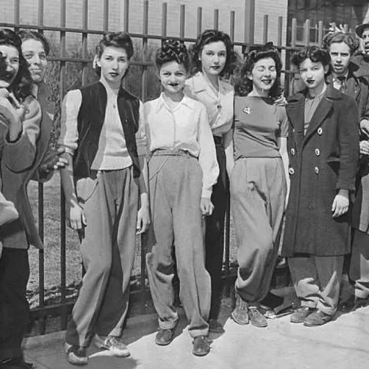 ankorinclan's tweet photo. La suspendieron por llevar pantalones azules y un jersey rojo. Al día siguiente, todo el instituto se presentó vestido igual que ella.

En marzo de 1942, Beverly Bernstein, de 16 años, fue enviada a casa desde su instituto en Brooklyn por llevar pantalones. La decana de estudiantes del Abraham Lincoln High School, Bertha Cohen, la suspendió por presentarse con pantalones de gabardina azul y "un jersey rojo carmín".

La suspensión, lejos de acabar el asunto, encendió la mecha. El periódico Brooklyn Daily Eagle planteó la pregunta a sus lectores el 26 de marzo de 1942: "¿Deberían las estudiantes de instituto, en particular las del Abraham Lincoln High School en Ocean Parkway, poder llevar pantalones a clase?". Al día siguiente de la suspensión, decenas de compañeras se presentaron en clase con pantalones en señal de solidaridad.

Las defensoras de Bernstein no argumentaron comodidad ni estilo. Argumentaron que los pantalones "son mejores que las faldas en caso de un ataque aéreo" y que eran vitales para "conservar las medias de seda", en plena Segunda Guerra Mundial, cuando el nailon y la seda se destinaban a la producción de paracaídas. Circularon una petición formal: "Las abajo firmantes desean obtener permiso oficial para llevar pantalones a la escuela porque el Gobierno de Estados Unidos defiende el uso de pantalones en la escuela, ya que son mejores que las faldas en caso de ataque aéreo, y porque frenan vestimentas demasiado provocativas".

En la fotografía aparecen, de izquierda a derecha, Roslyn Goldberg, Esther Cohen, Marian Hartman, Maryln Bodkin y Eleanor Groper, plantadas frente a la verja del instituto con los pantalones de sus padres y hermanos, convirtiendo una sanción disciplinaria en una protesta colectiva sobre quién decide cómo puede vestirse una adolescente.

📍 Fuente: Brooklyn Daily Eagle, 26 de marzo de 1942 / NY Daily News Archive, fotografía de Ben Sandhaus, Getty Images.