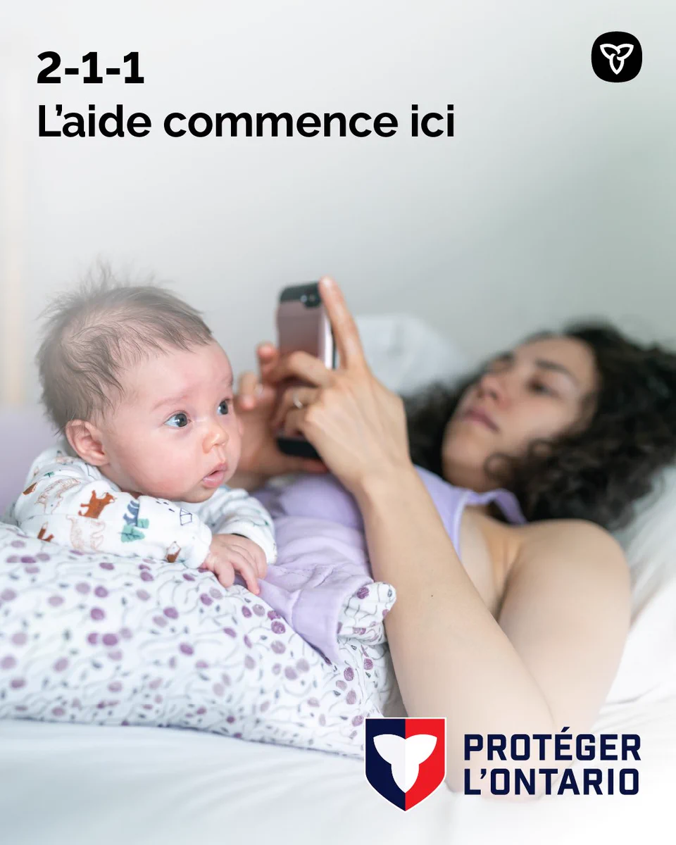 Personne aidante sur un lit utilisant un téléphone, avec un nourrisson à ses côtés. L’annonce fait la promotion de la ligne d’aide 211 avec le message : « L’aide commence ici. »