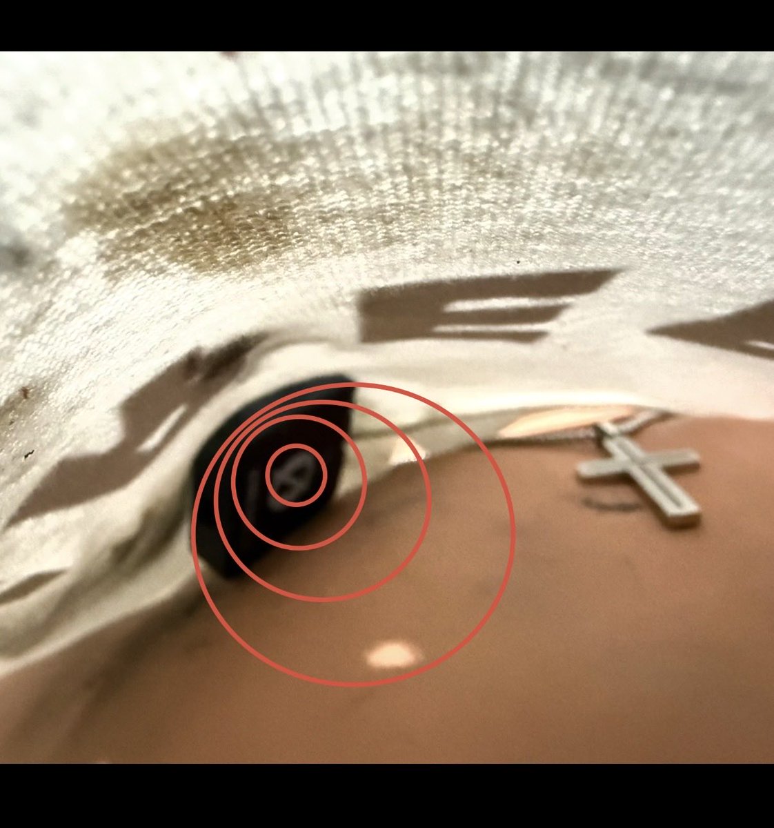 910Laser's tweet photo. Did the original plan assume the Rode mic would be lying flat on his chest?

If you look closely, the mic was tilted at an angle. Is it possible the force leaving the “flat shinny side” of the mic caused the necklace and shirt to lift quickly followed by a puncture into his neck from the edge of the cross as it and his chain was violently flying up and out of his shirt collar?