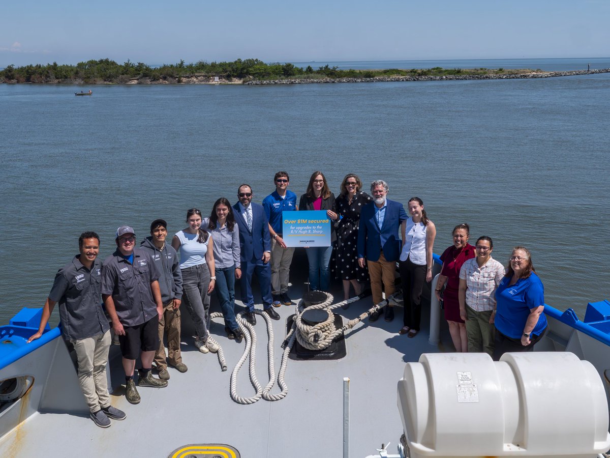 Rep. McBride, crew, and staff pose with a poster that reads "Over $1 million secured for upgrades to the R/V Hugh R. Sharp" on the hull of the ship. 