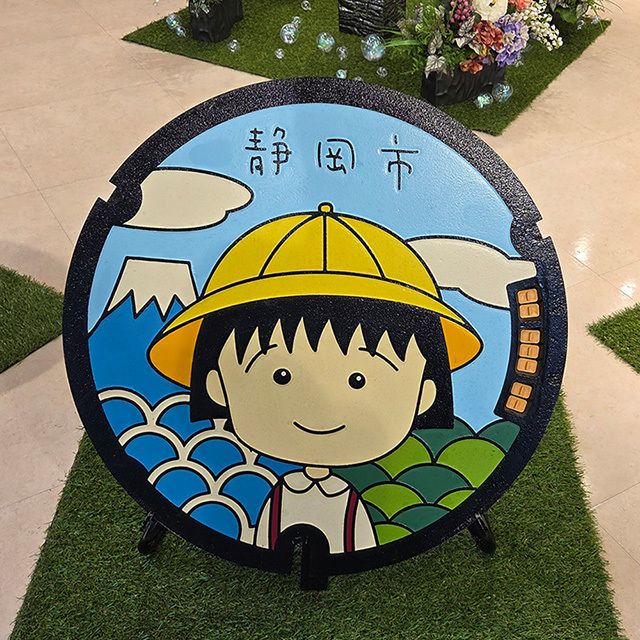 y_mochizuki's tweet photo. 静岡市で開催されたマンホールデザイン展。ちびまる子ちゃんのマンホールがひときわ目を引きます。沼津のラブライブ!サンシャイン!!のマンホールは色無しの鋳鉄そのままの姿で、逆に存在感あり。全国各地それぞれ、地域らしさが感じられました。
#手タレ #ハンドモデル #handmodel #マンホール https://t.co/Q1SAPeN7Tt
