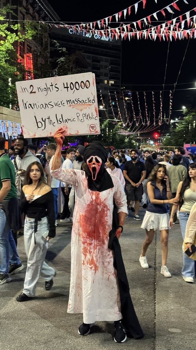 IranNewsAgency0's tweet photo. ⚡🇨🇦🦀پیام دادخواهی ایرانیان در میان جشن‌های فوتبالی ونکوور دیده شد/تصویری از یک شهروند ناشناس در خیابان‌های ونکوور کانادا در شبکه‌های اجتماعی بازتاب گسترده‌ای پیدا کرده است. این فرد با در دست داشتن پلاکاردی که روی آن نوشته شده «در ۲ شب، ۴۰ هزار ایرانی توسط جمهوری اسلامی قتل‌عام شدند» تلاش کرد توجه افکار عمومی را به سرکوب و کشتار گسترده ایرانیان جلب کند. انتشار این تصویر در میان فضای شاد جشن‌های فوتبالی، به نمادی از تلاش ایرانیان برای شکستن سکوت جهانی و زنده نگه داشتن حافظه قربانیان تبدیل شده است.