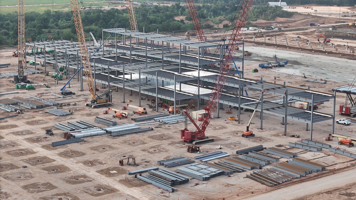 JoeTegtmeyer's tweet photo. Construction of the @Tesla Optimus Factory at Giga Texas (planned for ~10M/yr production once fully ramped up) continues, with more of the steel structure assembly evident. The structure appears to have (at least in this section) 4 floors, but that could vary across the entire factory as assembly continues.

More footings have been completed, GeoPier work on the N end while grade work on the S end. Land reclamation work also on the far S end to extend the ground slab of the building further.

Lots of work ahead, but I think they are currently on track for a late 2027 substantive completion of the structure. However, I would not be surprised to see initial setup & test production underway before the building itself is fully completed, just like we saw with the original main factory.