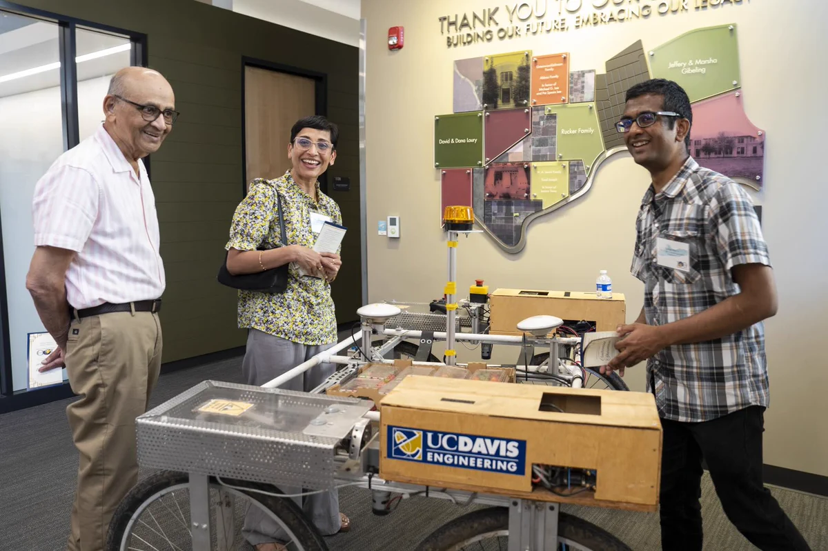 Two attendees smile with Ph.D. student Daniel
Martin while he exhibits the Fragile Crop Harvest-
Aiding Mobile Robot (FRAIL-Bot).