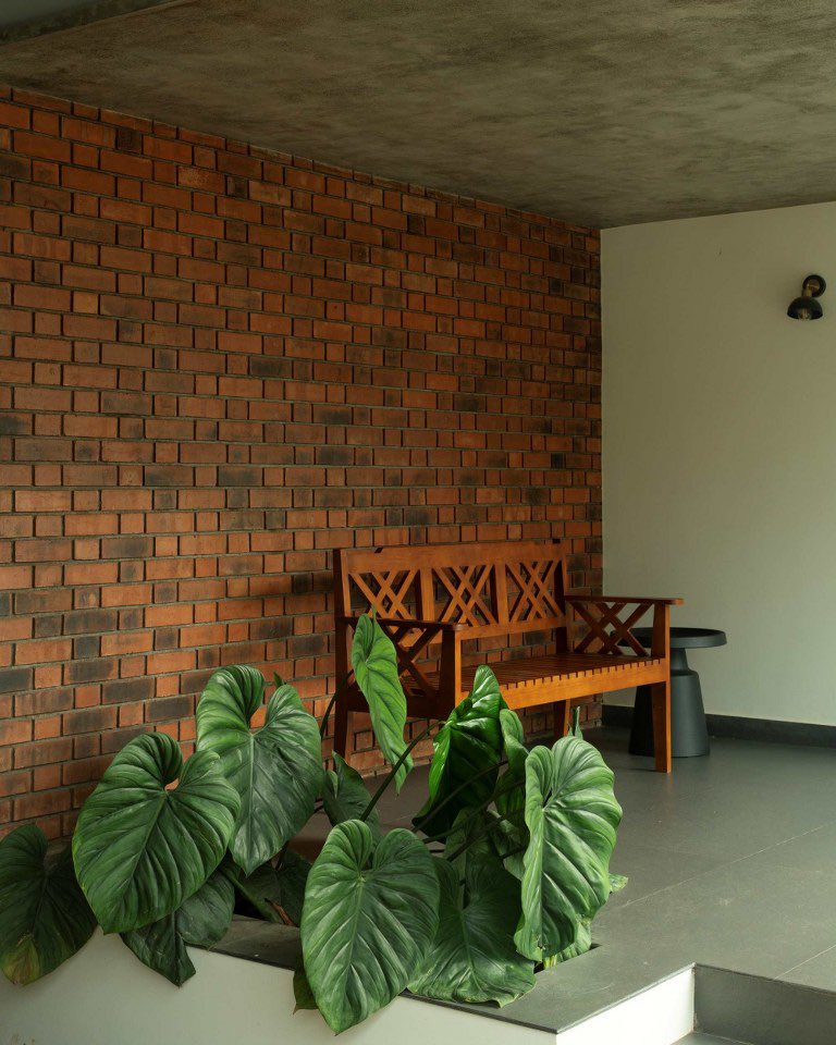 shavnyuy's tweet photo. This is what it looks like when an architect refuses to apologize for where they are.

Beth Eden in Wayanad, Kerala sits on a linear plot surrounded by rubber trees and palms, and every material used to build it is left exactly as it arrived: exposed red brick, raw concrete ceilings, solid teak wood crafted by local carpenters into doors, shutters, wall panelling and furniture. The gabled roof projections mark the entrance and living zones without ornamentation. The generous overhangs handle the monsoon without asking anything extra from the structure.

The veranda has a bench and a plant. That’s the whole design decision. Brick wall behind it, concrete above it, teak in front of it. Nothing performing. Nothing pretending.

Inside, the vaulted ceiling follows the gable profile exactly as it was built. The living room teak was custom made. The windows were made by local carpenters. The house cost what it cost because the labor and materials were already there.

Africa has laterite in the ground, hardwood in the forest and craftsmen who know exactly what to do with all of it, and what we need is not another glass tower in a capital city but more brick kilns producing standard fired brick at scale so that our architects stop reaching for cement blocks every time they need a wall.

Design: Forge and Furnish | Ar. Liz Tomy | Sulthan Bathery, Wayanad

More images in the comments.