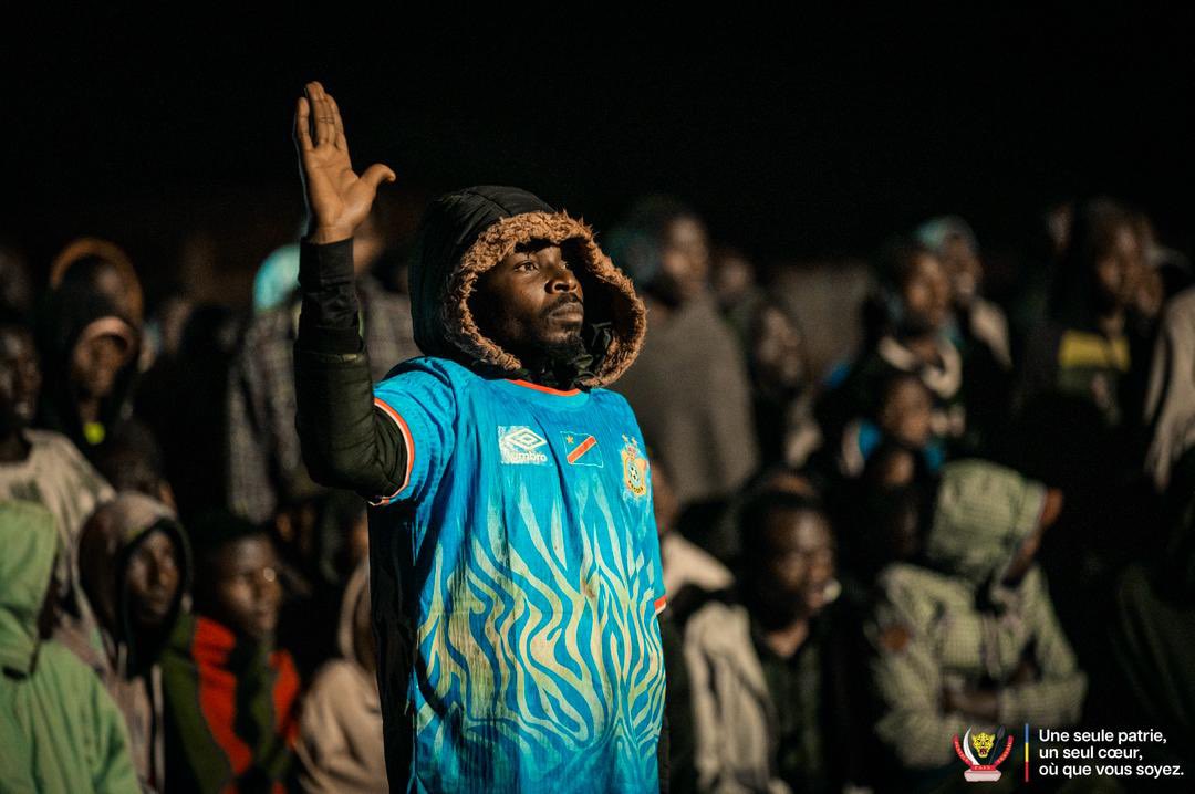 michombero's tweet photo. #Kinama : à l’aube glaciale de l’exil, les réfugiés congolais vibrent au rythme des Léopards

Il est à peine 4 heures du matin lorsque les premiers réfugiés congolais commencent à converger vers le site de retransmission installé au camp de Kinama. Malgré le froid mordant qui enveloppe les collines du nord-est du Burundi, des centaines d’hommes, de femmes et d’enfants se mobilisent pour suivre le match de Coupe du monde opposant la RDC à la Colombie.

Munis de chaises, emmitouflés dans des couvertures ou vêtus des couleurs nationales, dans le cadre d’un bon voisinage, d’autres Burundais qui supportent les Léopards parcourent parfois plusieurs kilomètres à pied pour vivre ce rendez-vous avec la sélection nationale. Dans ce camp qui accueille plus de 6000 Congolais ayant fui les violences dans l’est de la RDC, l’événement dépasse largement le cadre sportif.

Avant le coup d’envoi, l’ambiance est marquée par les chants, les pronostics et une grande ferveur patriotique. Chaque action des Léopards est suivie avec passion, chaque occasion suscite l’espoir d’un exploit face à la Colombie.

Malgré la défaite congolaise (1-0), les réfugiés ne cachent pas leur fierté. Très vite, les discussions se tournent vers le prochain match contre l’Ouzbékistan. Pour beaucoup, l’essentiel était ailleurs : se retrouver, partager un moment d’unité et rester connectés à leur pays d’origine.

Au camp de Kinama, cette nuit a une nouvelle fois démontré la résilience des réfugiés congolais. Loin de leur terre natale, mais toujours attachés à la RDC, ils ont rappelé que l’exil n’efface ni l’identité, ni l’espoir, ni l’amour de la patrie.